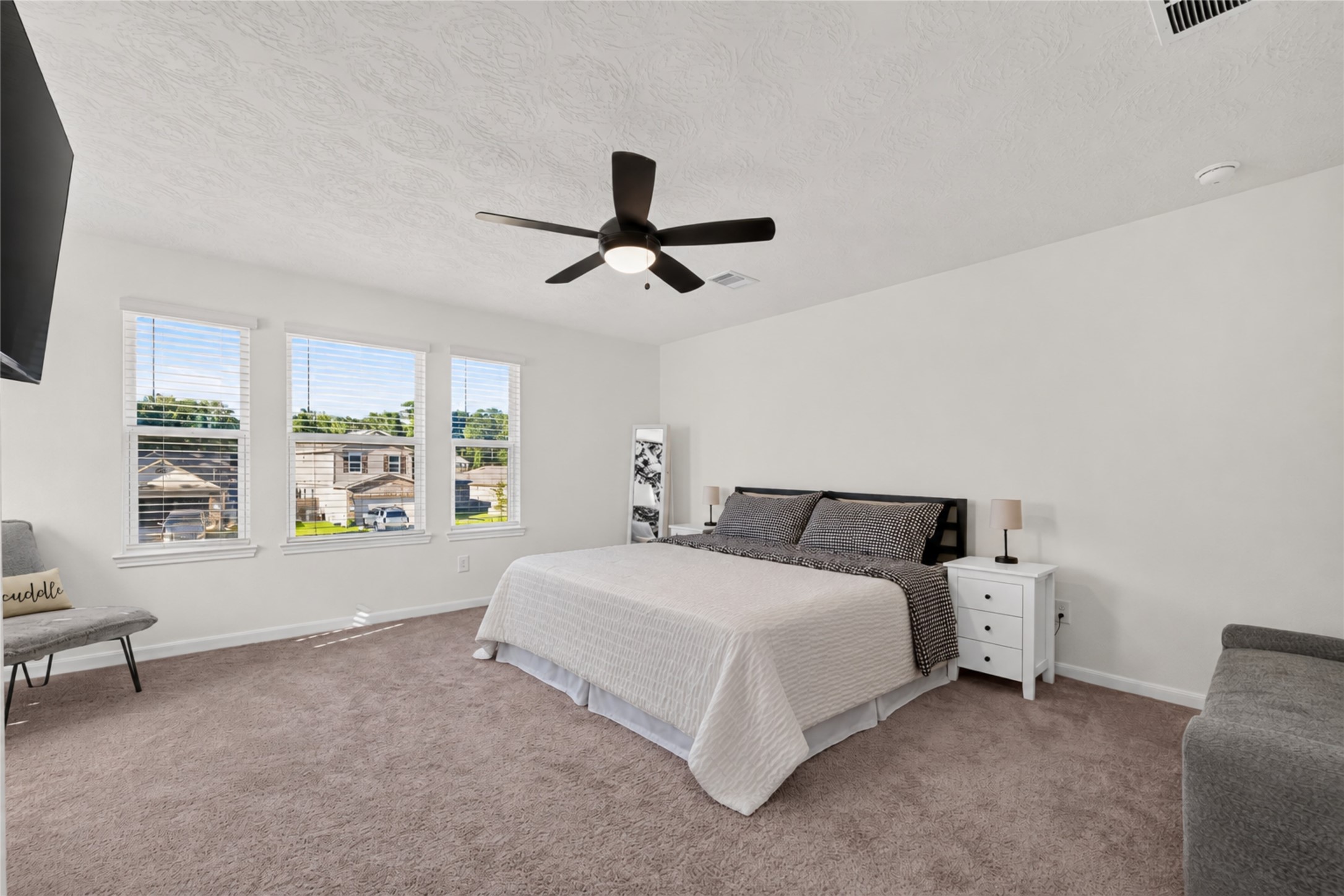 Retreat to this spacious primary bedroom featuring soft carpeting, a ceiling fan, and multiple windows that welcome natural light. The generous layout provides a comfortable setting for relaxation and restful evenings.