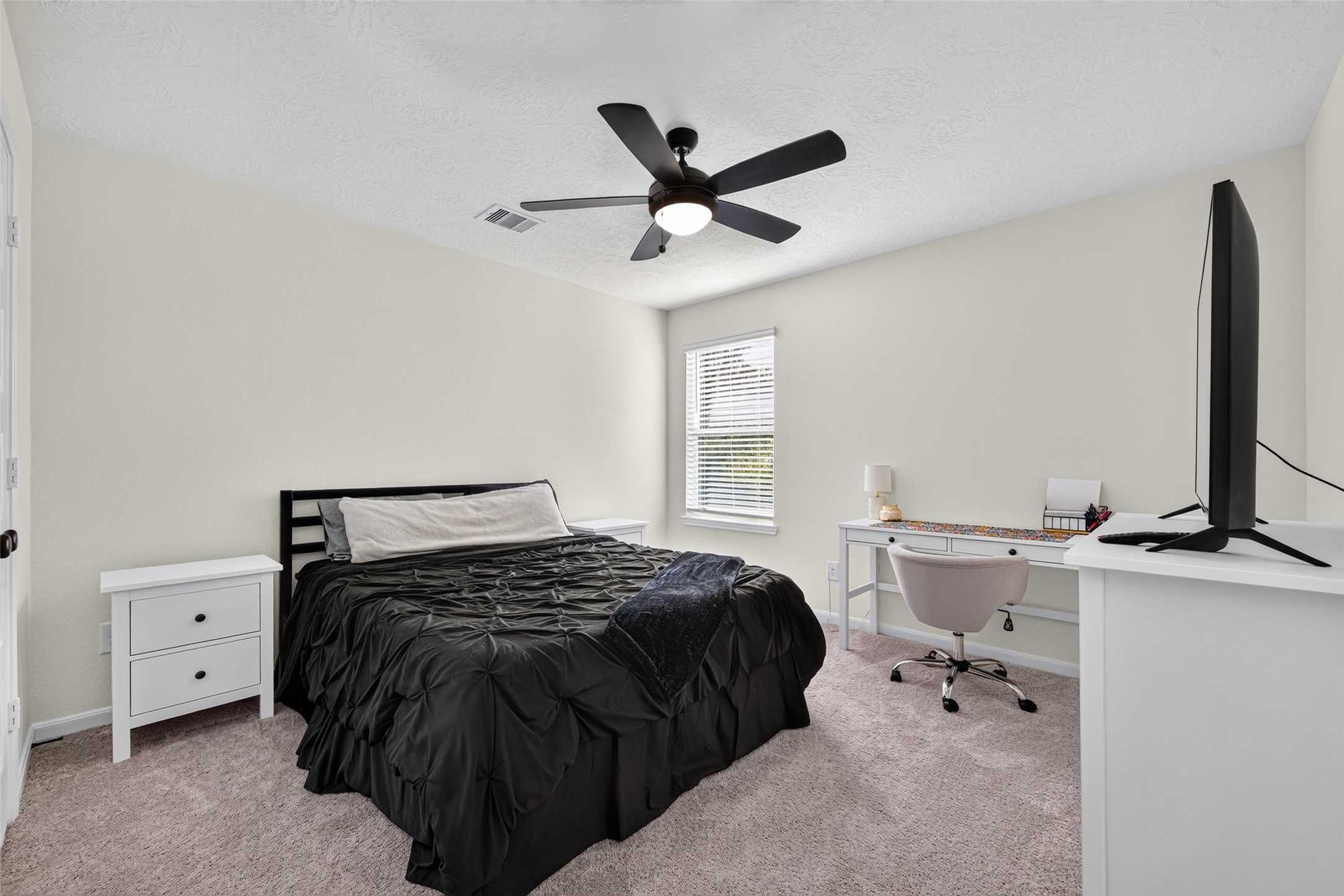 This inviting secondary bedroom offers a comfortable setting with soft carpeting and natural light. Its neutral finishes provide the perfect backdrop for creating a restful retreat or personalized living space.