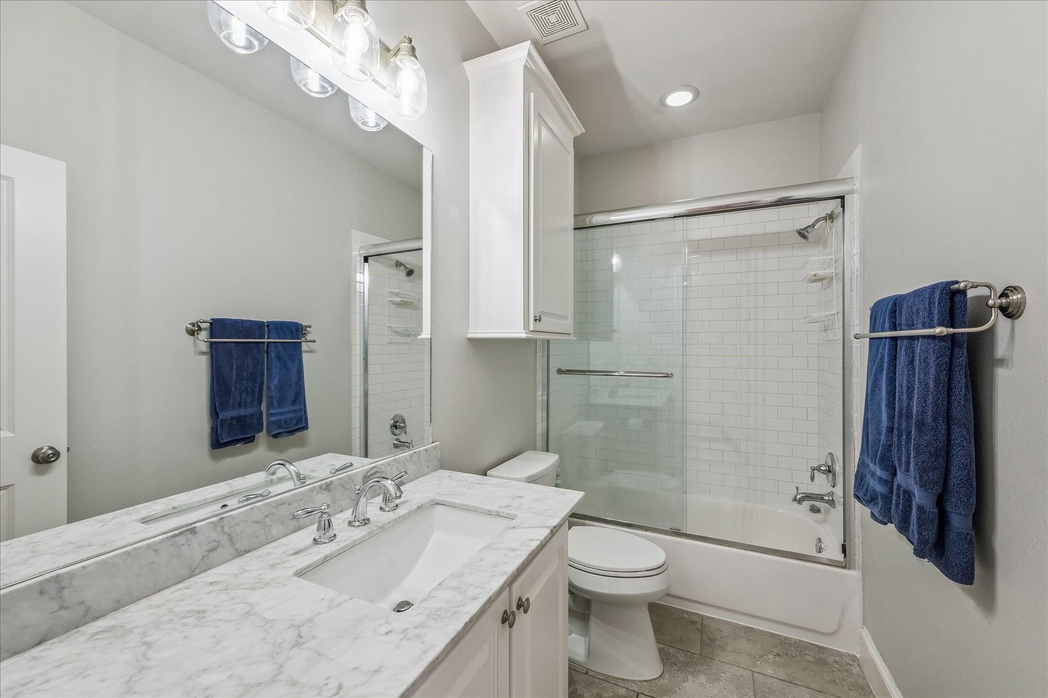 Upstairs full bathroom with modern fixtures, a glass-enclosed shower-tub combo, ample storage and a bright, clean aesthetic