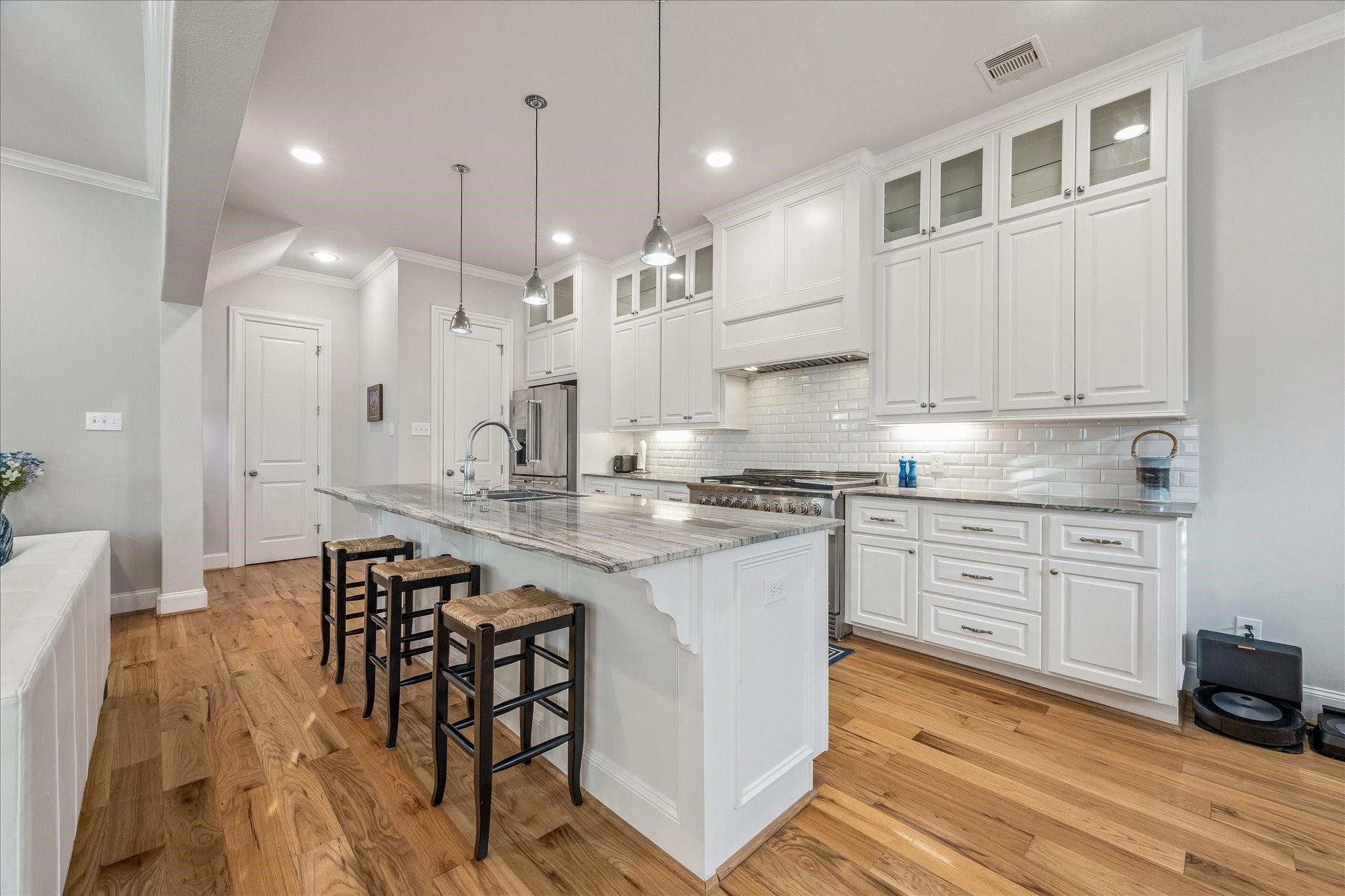 This modern kitchen features custom cabinetry, beautiful quartz countertops, and a large island with seating to gather around. The pendant lighting, subway tile backsplash and glass accents add a clean, stylish touch.