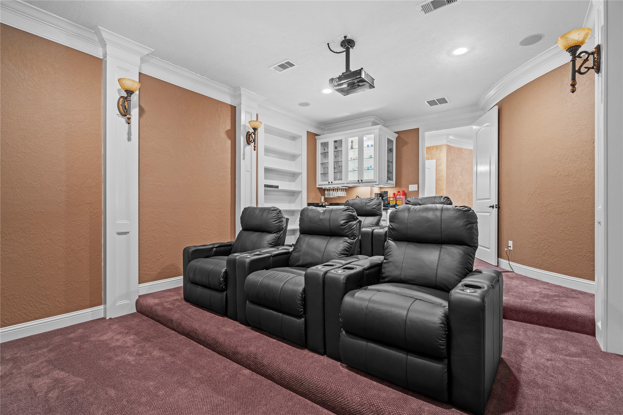 Home theater showcasing tiered leather seating, a ceiling-mounted projector, built-in cabinetry, and a convenient refreshment bar.