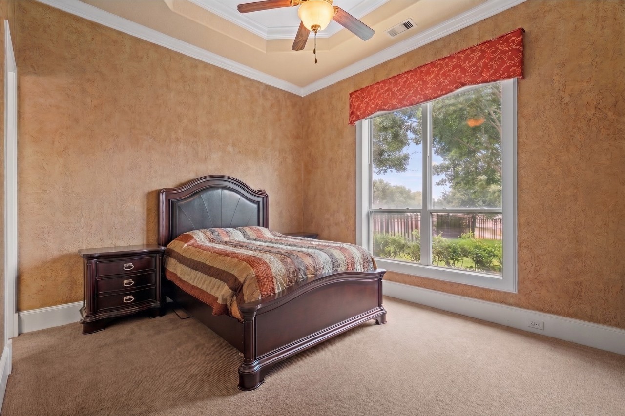 Spacious second bedroom featuring a tray ceiling, generous natural light, and serene views of the landscaped grounds.