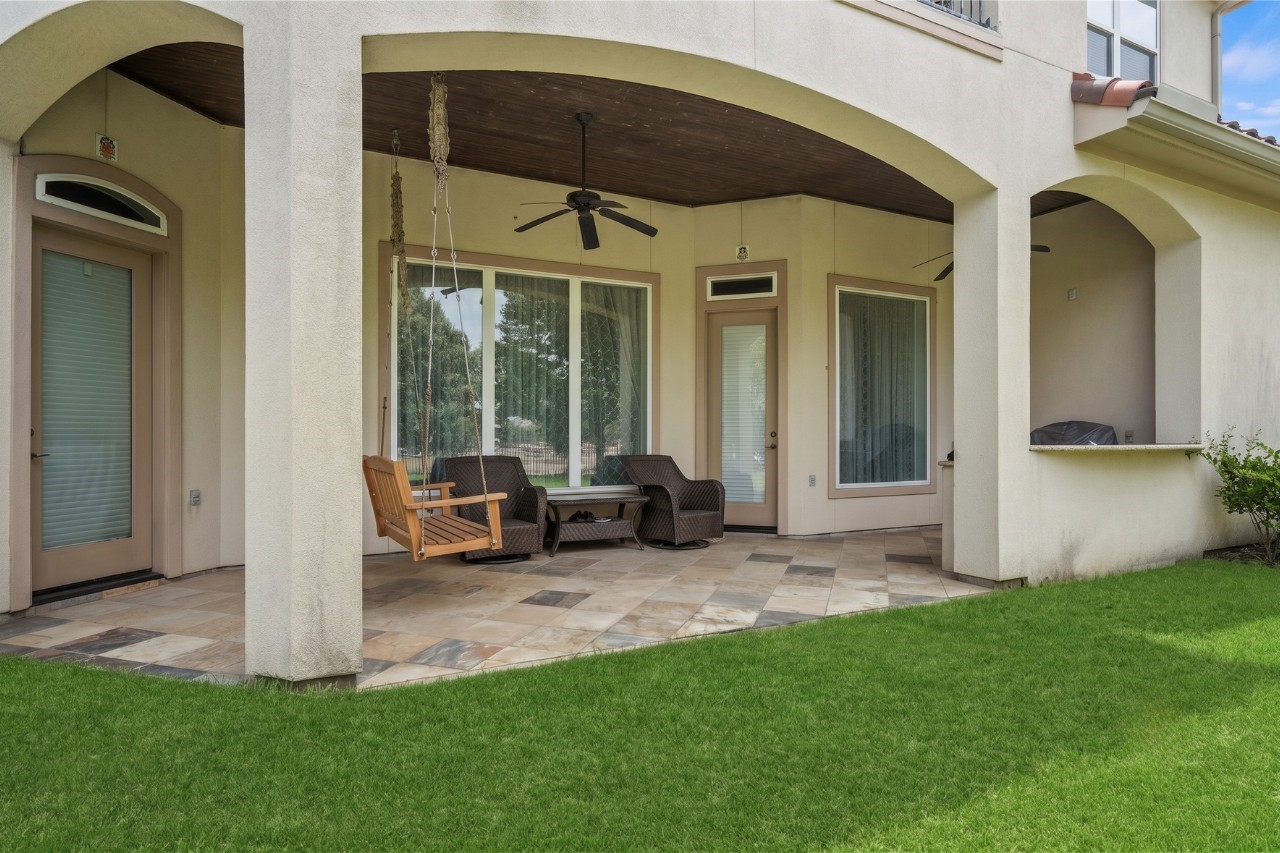 Rear exterior view showcasing a spacious backyard, covered patio, upper-level balcony, and attractive arched architectural details.