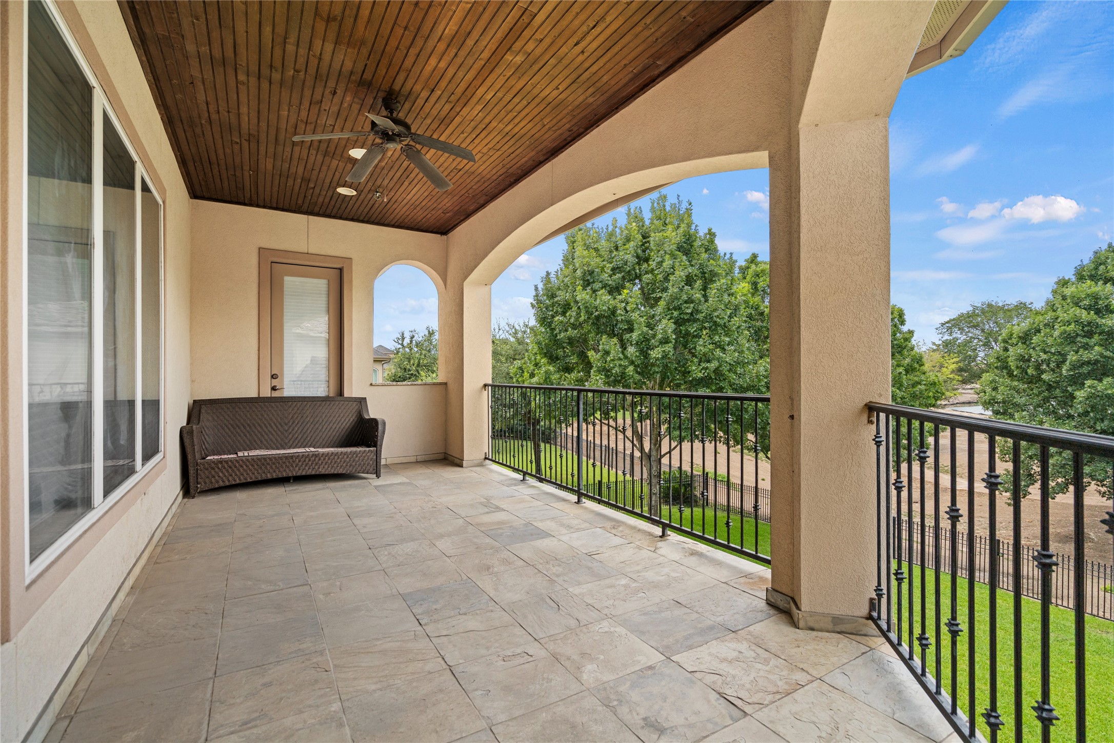 Spacious covered patio featuring elegant columns, a wood-paneled ceiling, and serene views of the lush surrounding landscape.