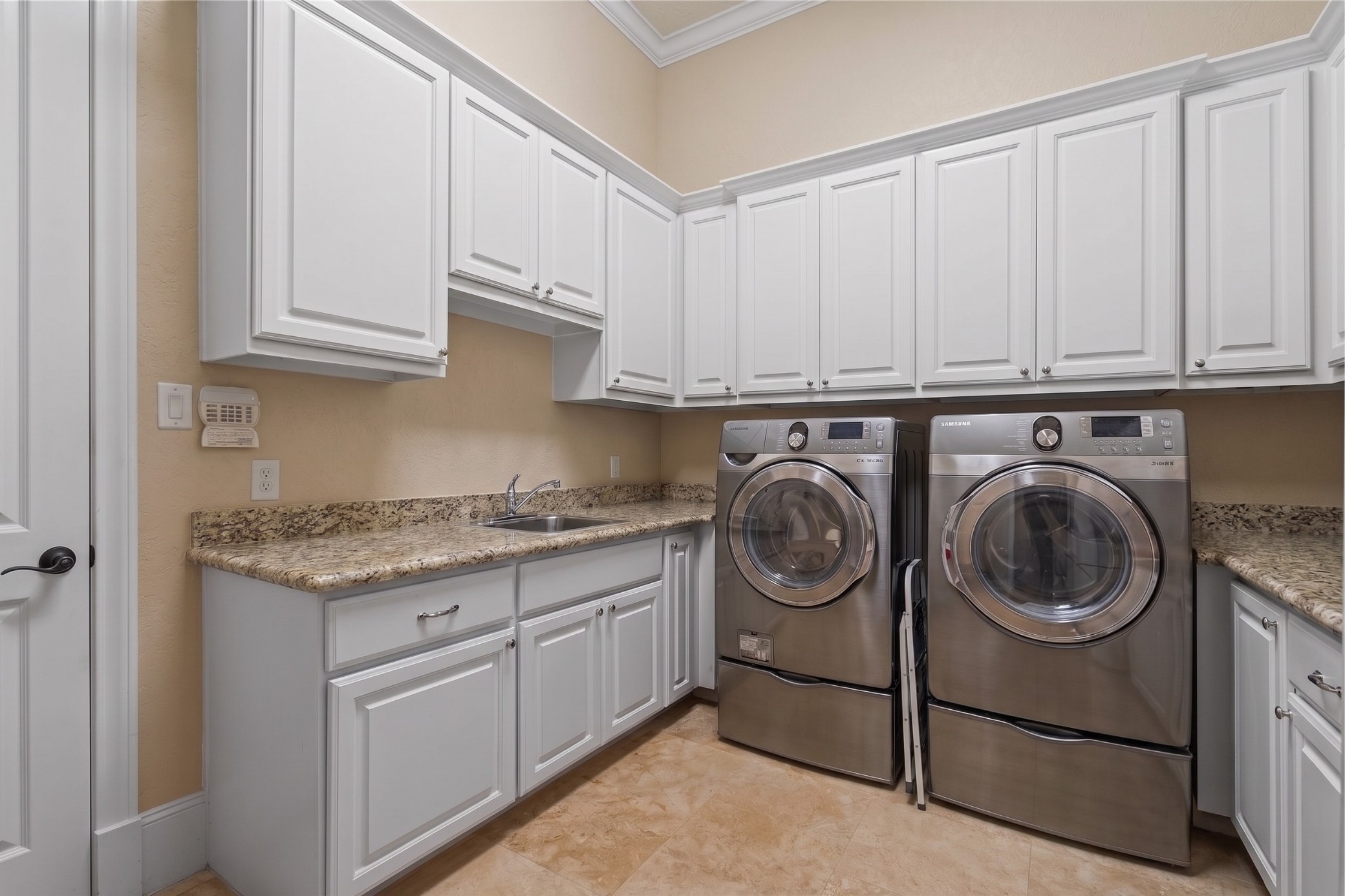 Generously sized utility room featuring extensive cabinetry, granite countertops, a built-in sink, and ample workspace for everyday convenience.