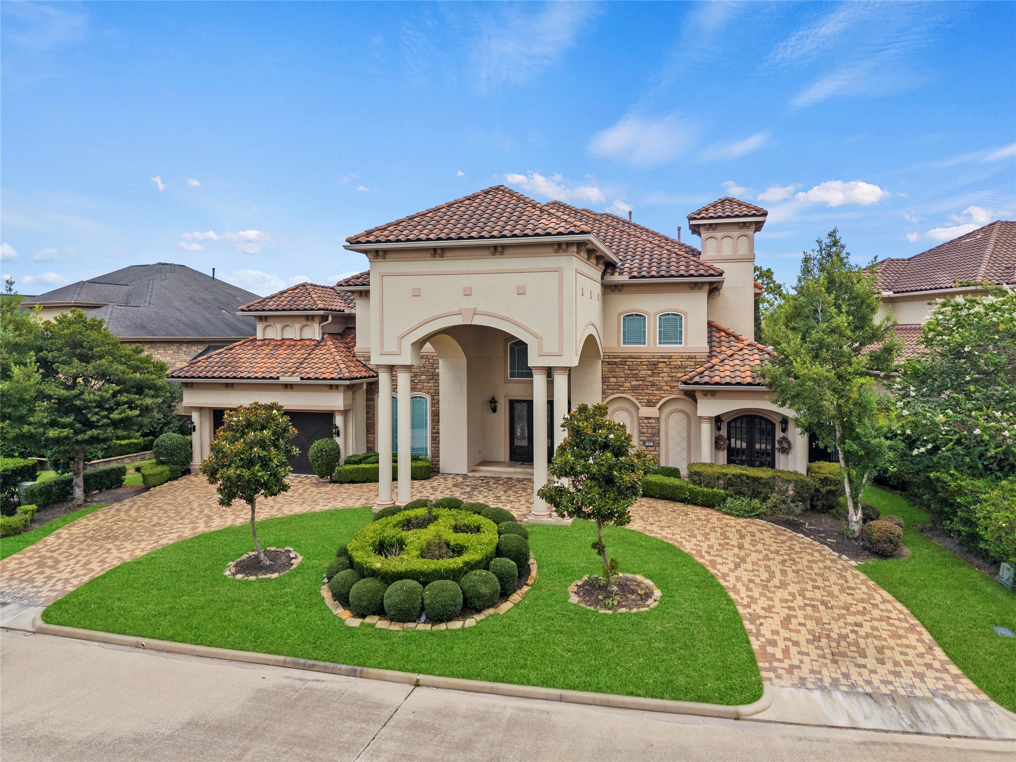 A commanding front elevation highlights refined stonework, an impressive arched entry, and sculpted landscaping for a luxury presence.