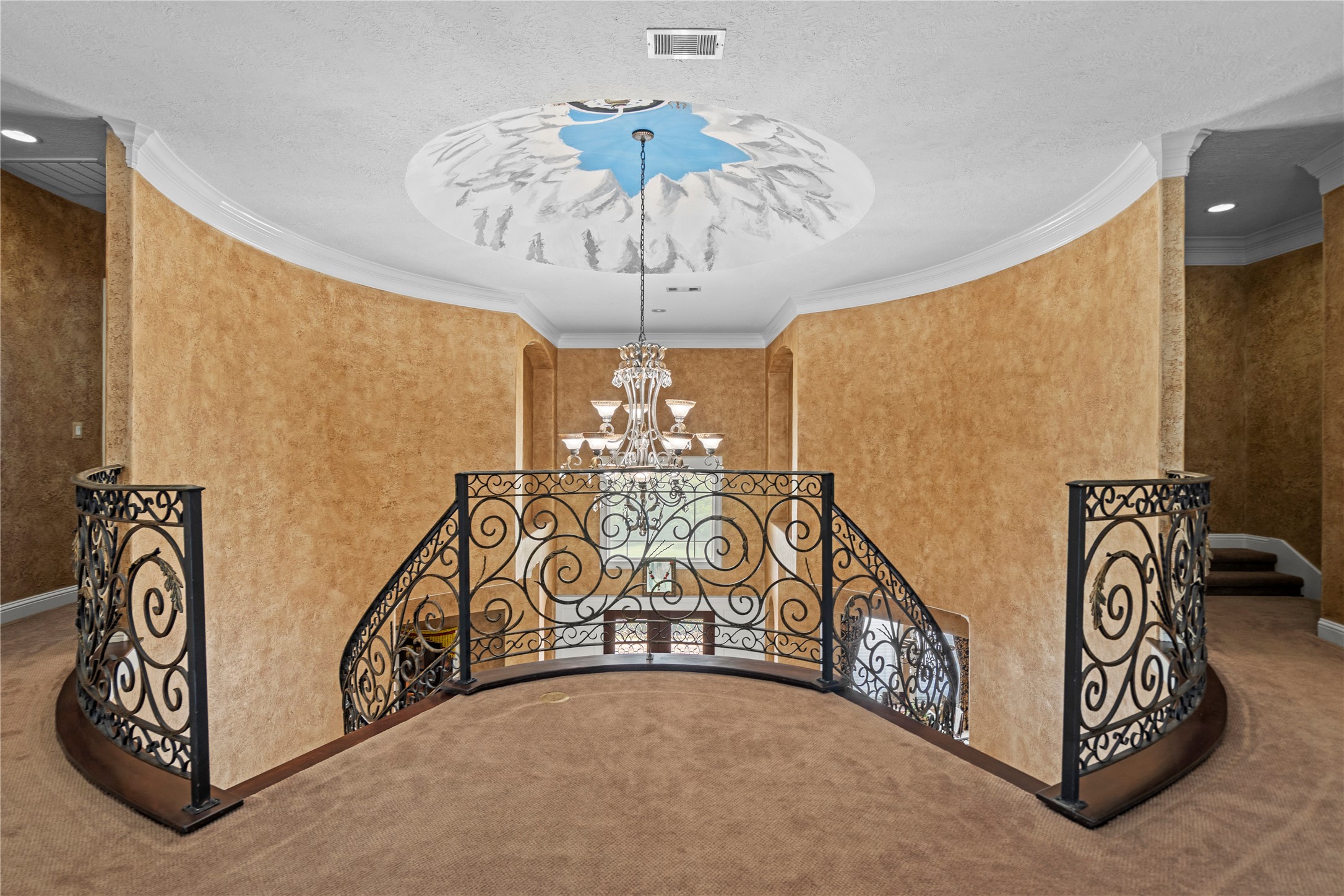 Elegant second-floor landing overlooking the grand foyer, featuring wrought-iron railings, a statement chandelier, custom painted dome and distinctive architectural details.