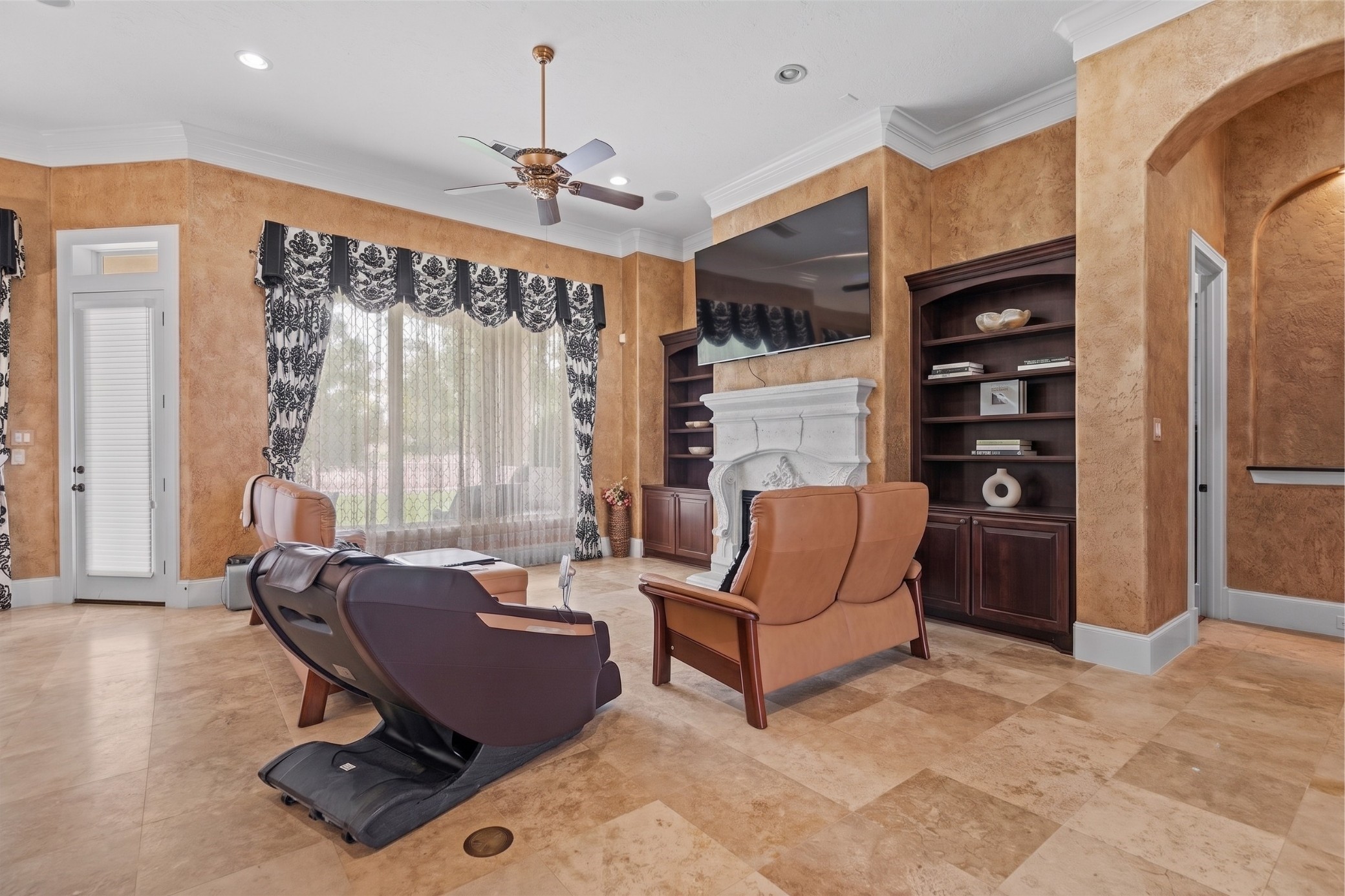 Living area featuring an ornate stone fireplace, custom built-in cabinetry, and windows that fill the space with natural light.