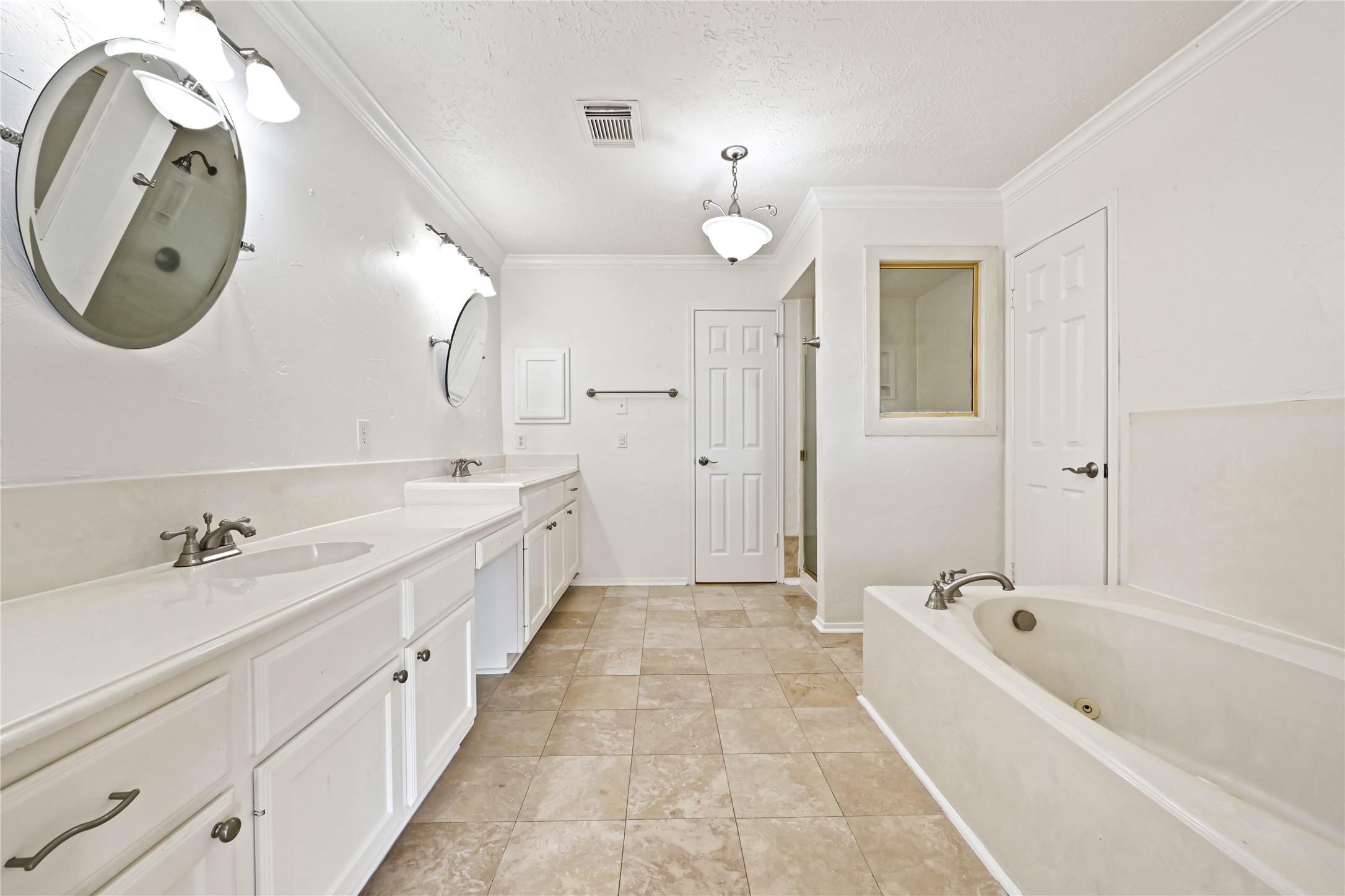 Ample space bathroom featuring dual sinks, elegant fixtures, a luxurious soaking tub, and a separate shower, all set against tasteful tile flooring.