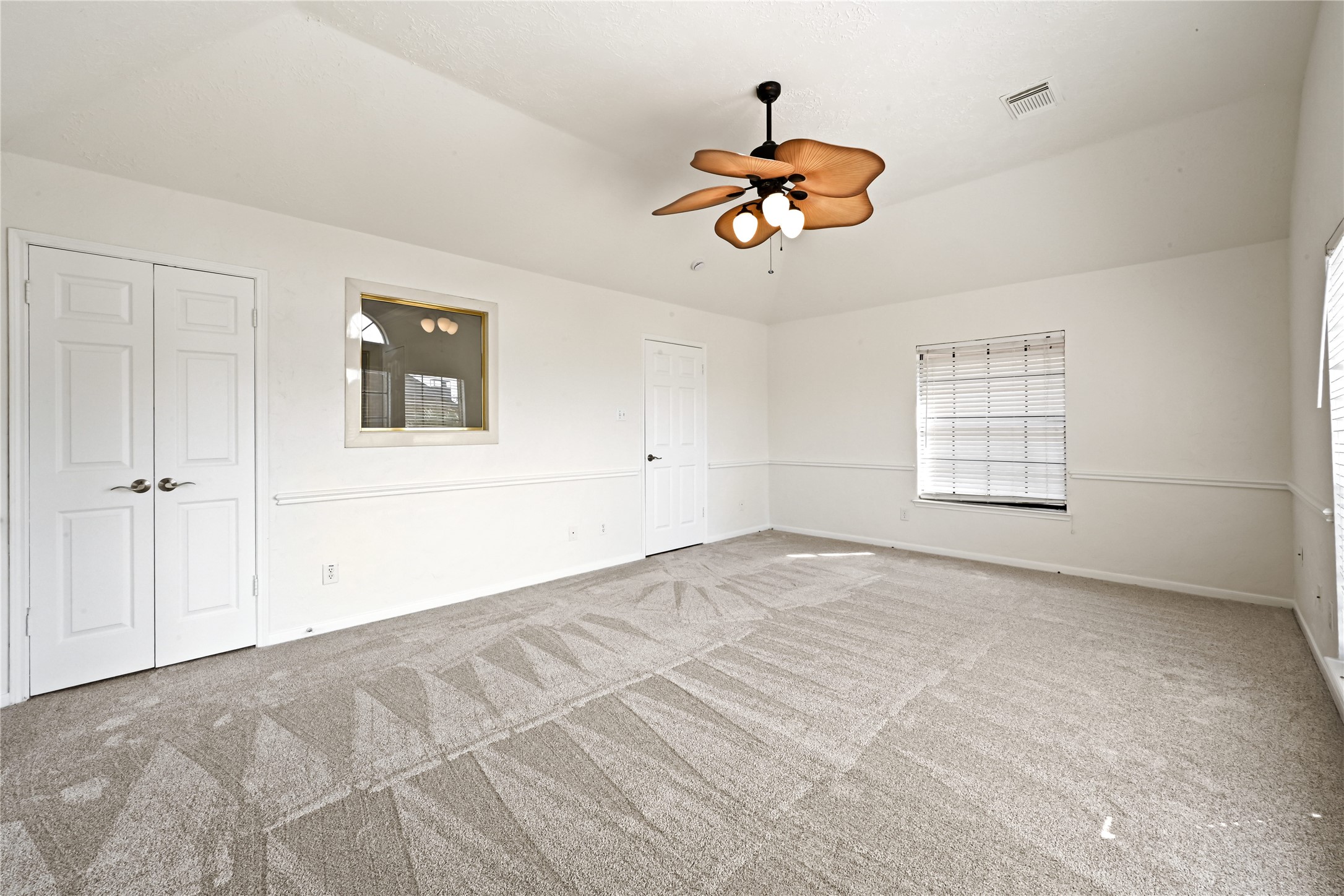 Spacious bedroom with fresh carpeting, a unique ceiling fan, and abundant natural light from multiple windows.