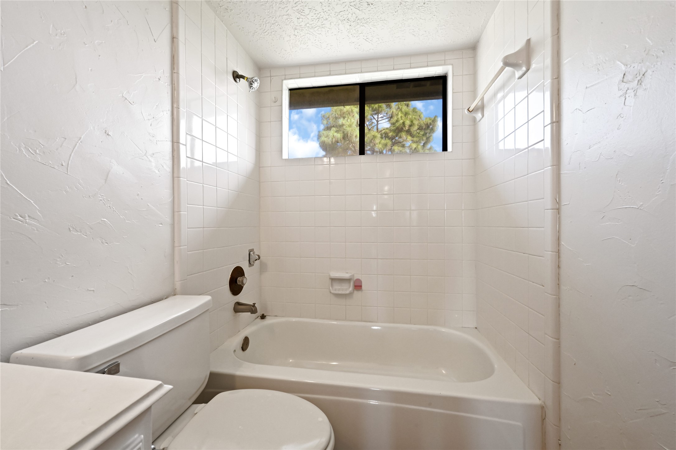 Bright bathroom featuring a classic white tile bathtub with a window above, providing natural light and a serene view.