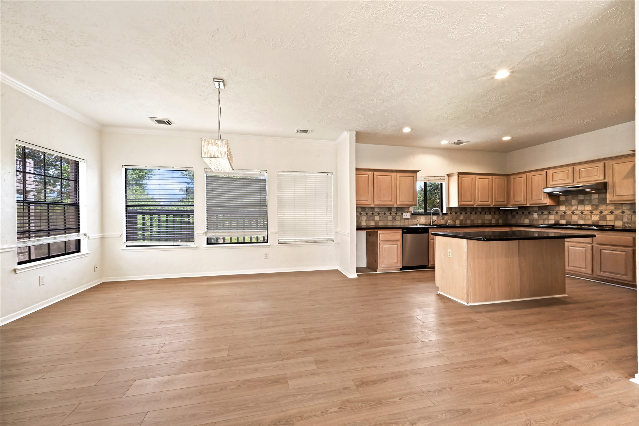 Spacious open-concept kitchen and dining area featuring warm wood floors, abundant natural light from multiple windows, modern pendant lighting, and ample cabinetry with a large central island perfect for gatherings.