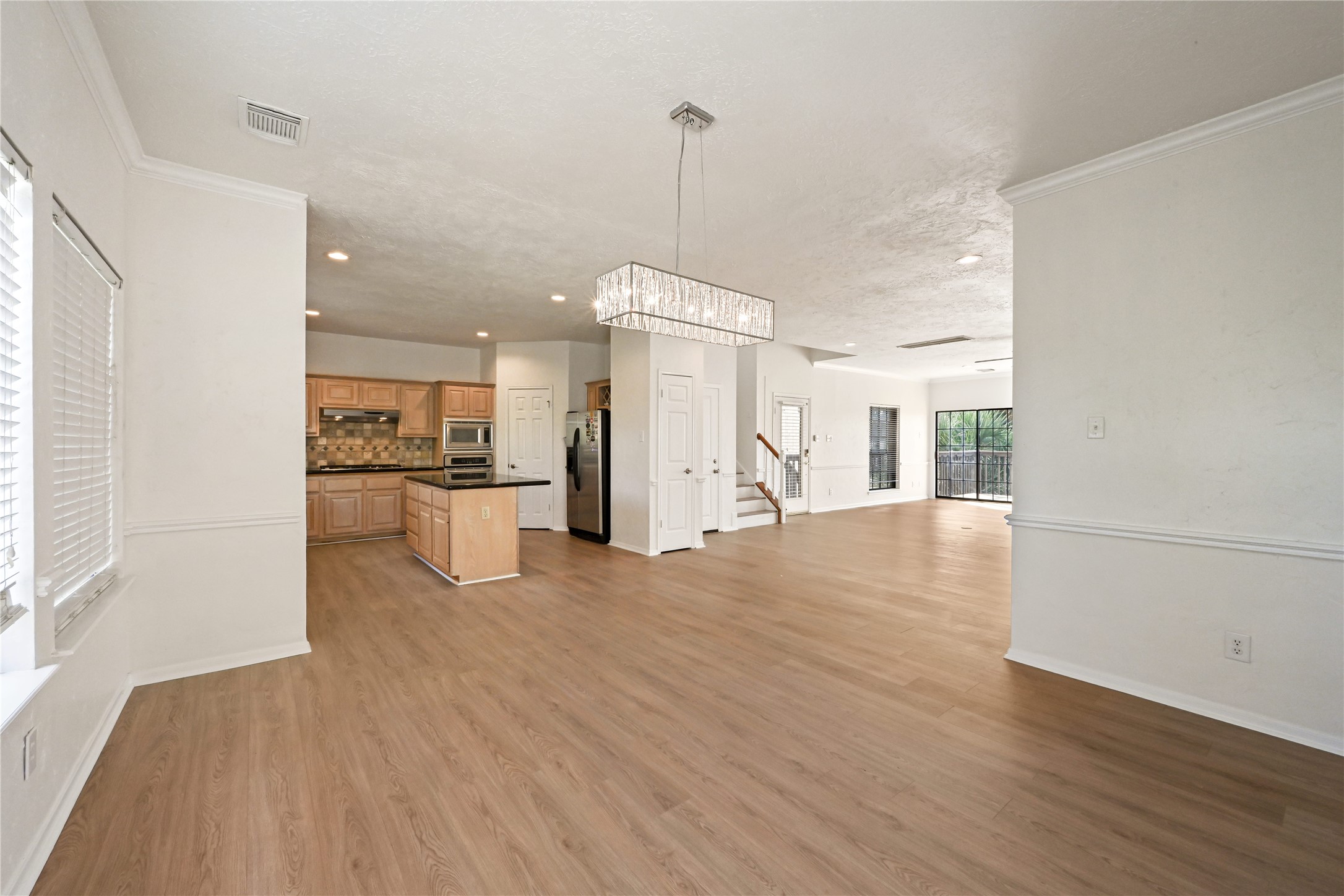 Spacious open-concept living area featuring elegant hardwood floors, a modern chandelier, and a sleek kitchen with ample cabinetry and stainless steel appliances.