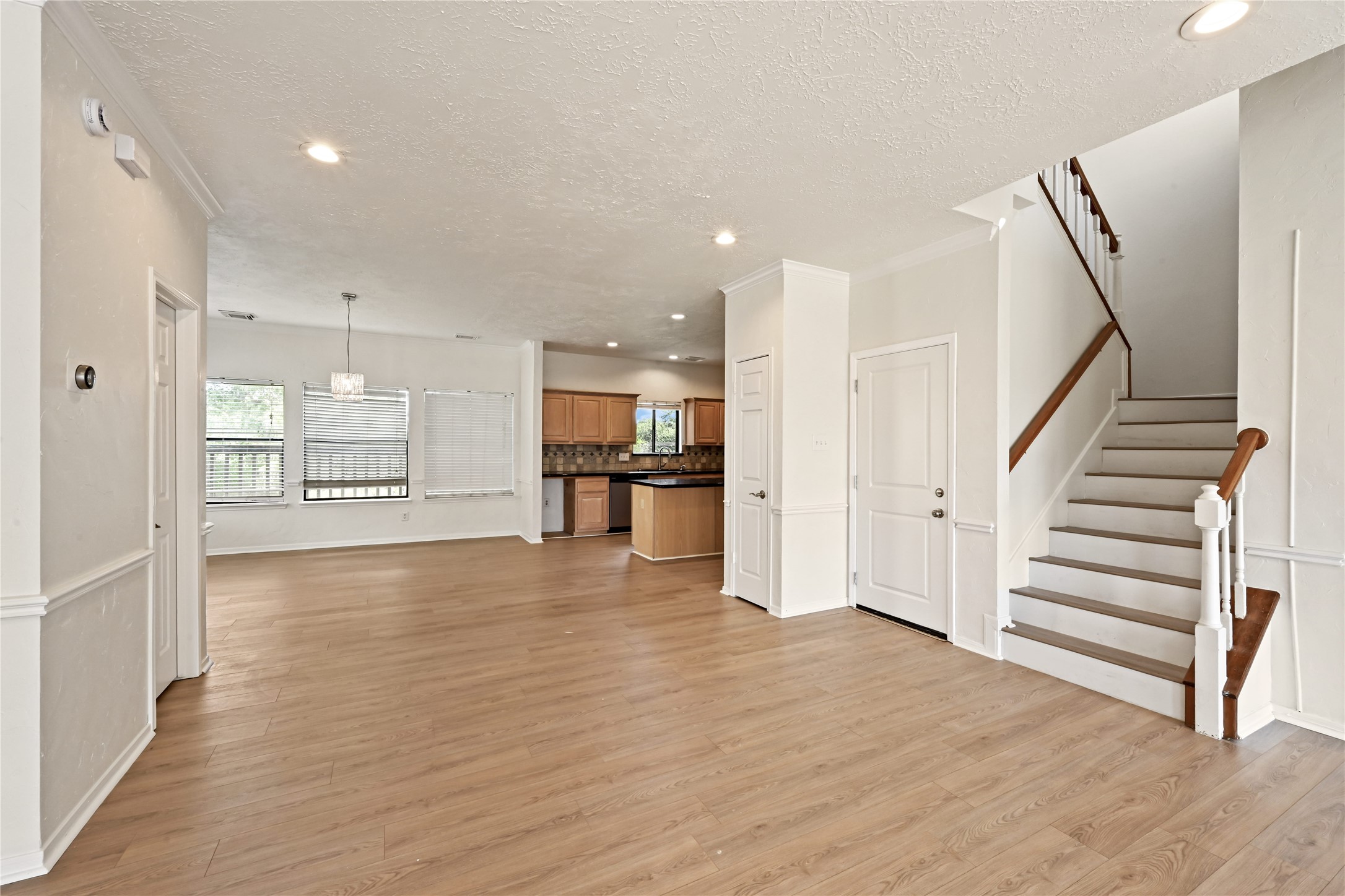 Spacious open-concept living area with elegant wood flooring, abundant natural light, and a modern kitchen featuring warm cabinetry. The staircase leads to the upper level, adding a touch of sophistication.