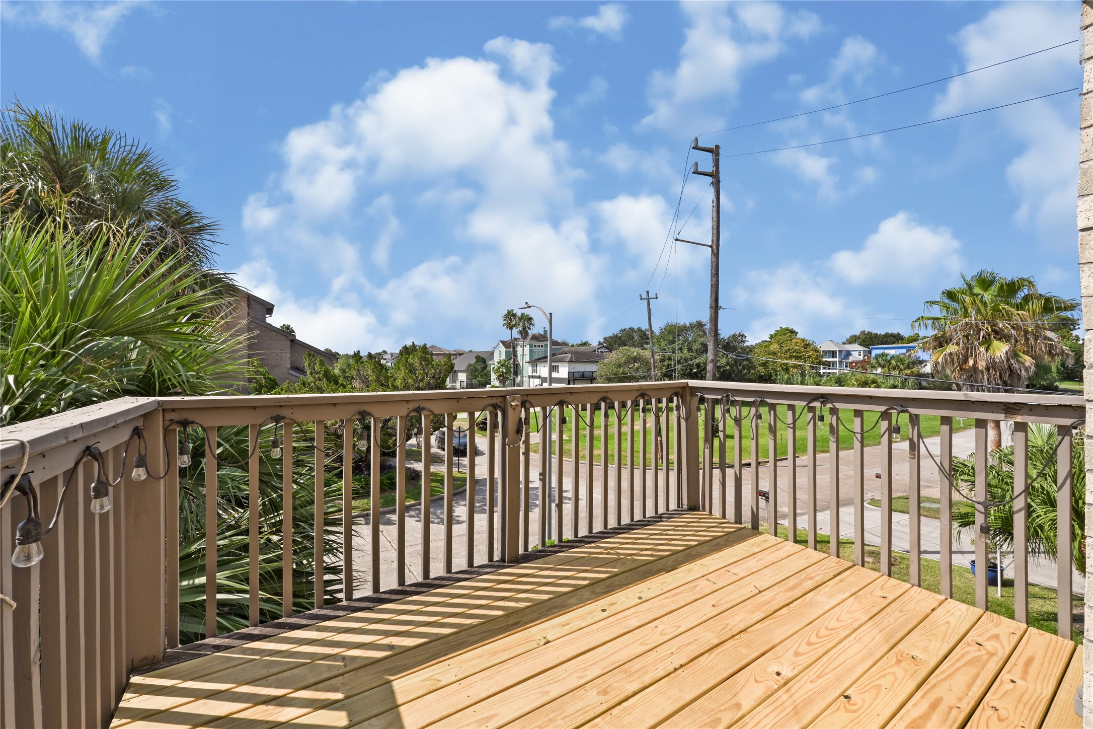 Enjoy serene views from this inviting wooden deck, perfect for relaxing and entertaining, surrounded by lush greenery and bright blue skies.