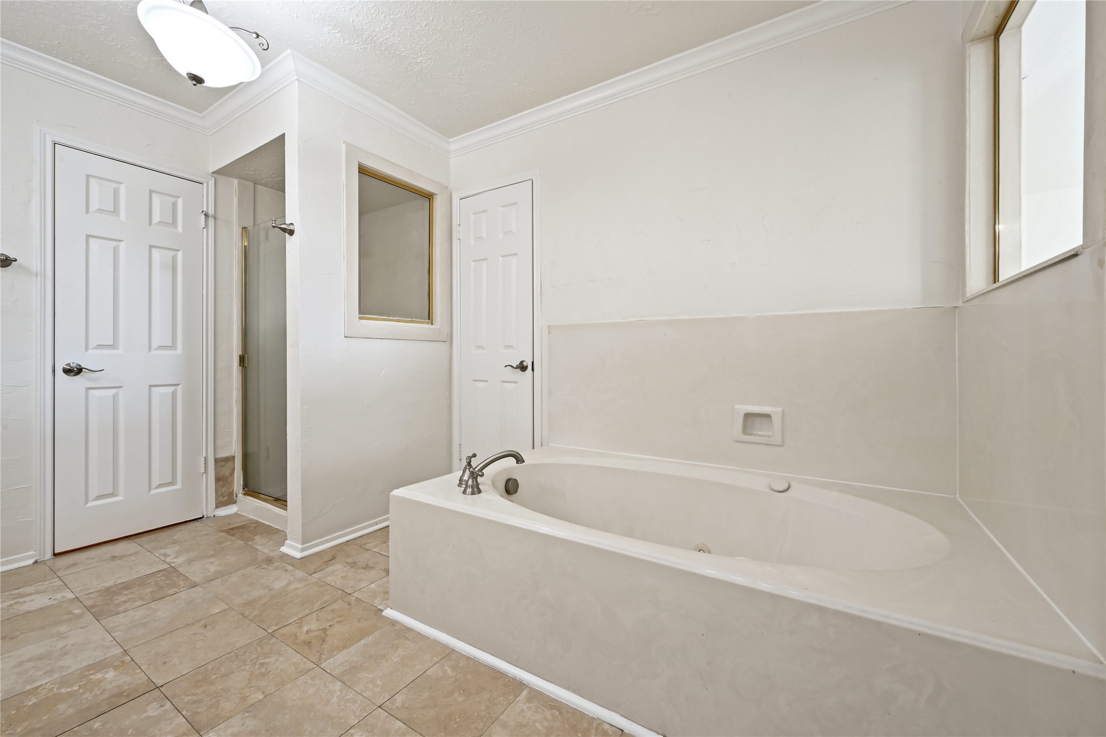 Spacious bathroom featuring a luxurious soaking tub, separate glass-enclosed shower, and elegant tile flooring, offering a serene retreat.