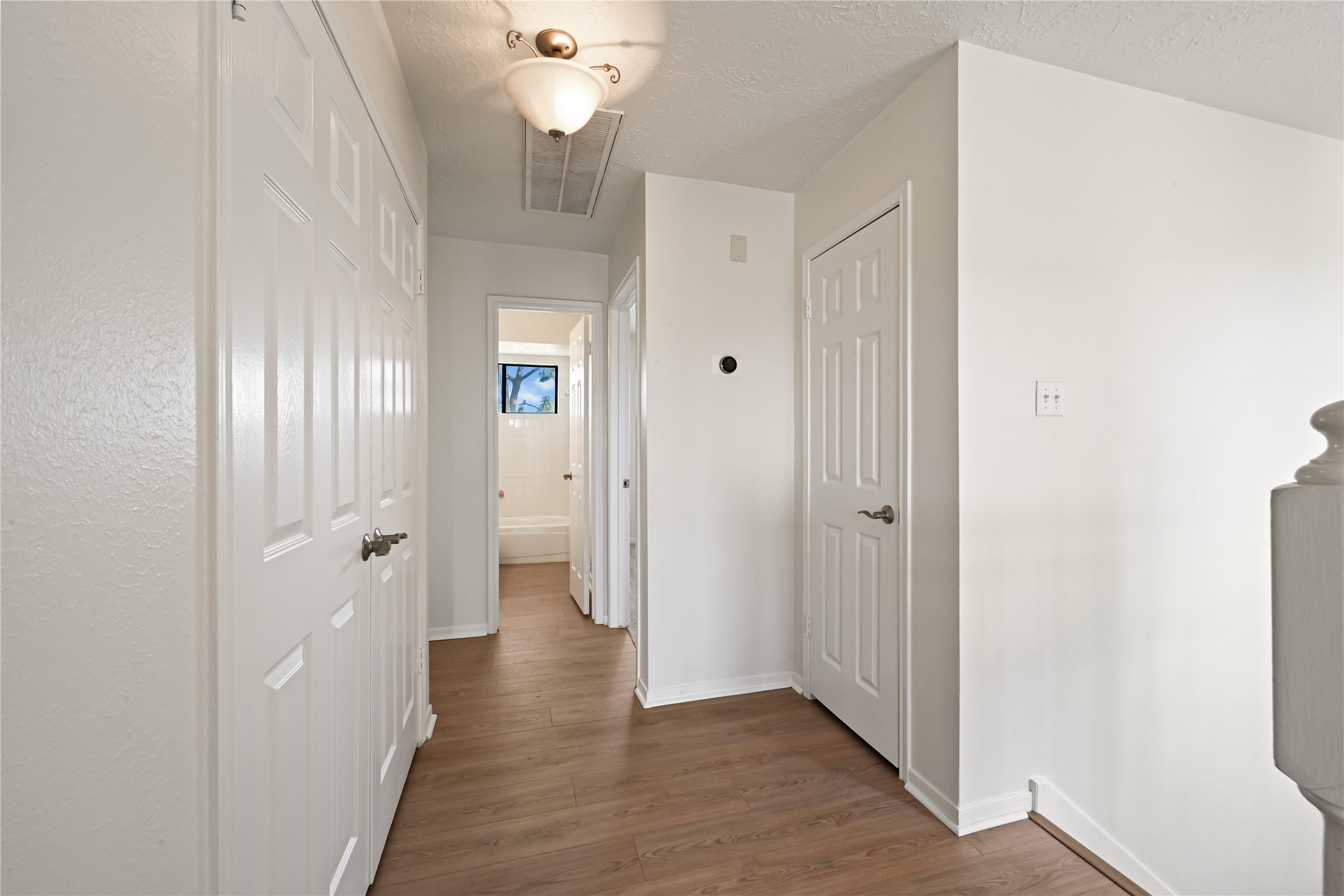 Bright and welcoming hallway with sleek hardwood floors, modern light fixture, and multiple doorways leading to spacious rooms.