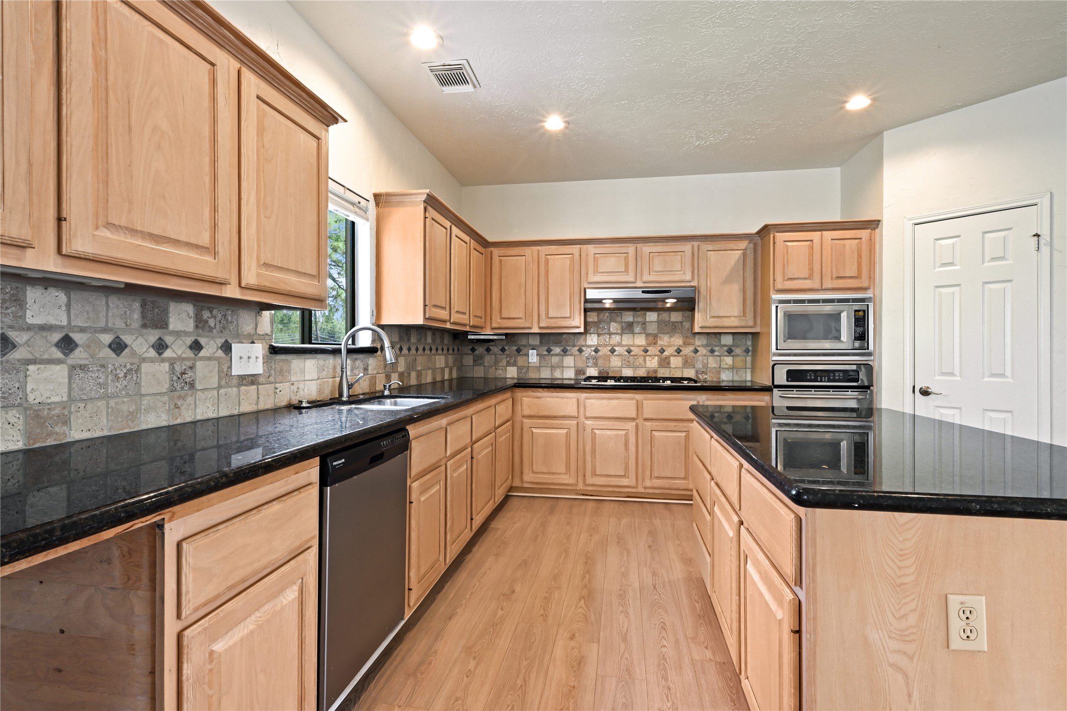 Kitchen features sleek black granite countertops, abundant light wood cabinetry, and modern stainless steel appliances, perfect for culinary enthusiasts.