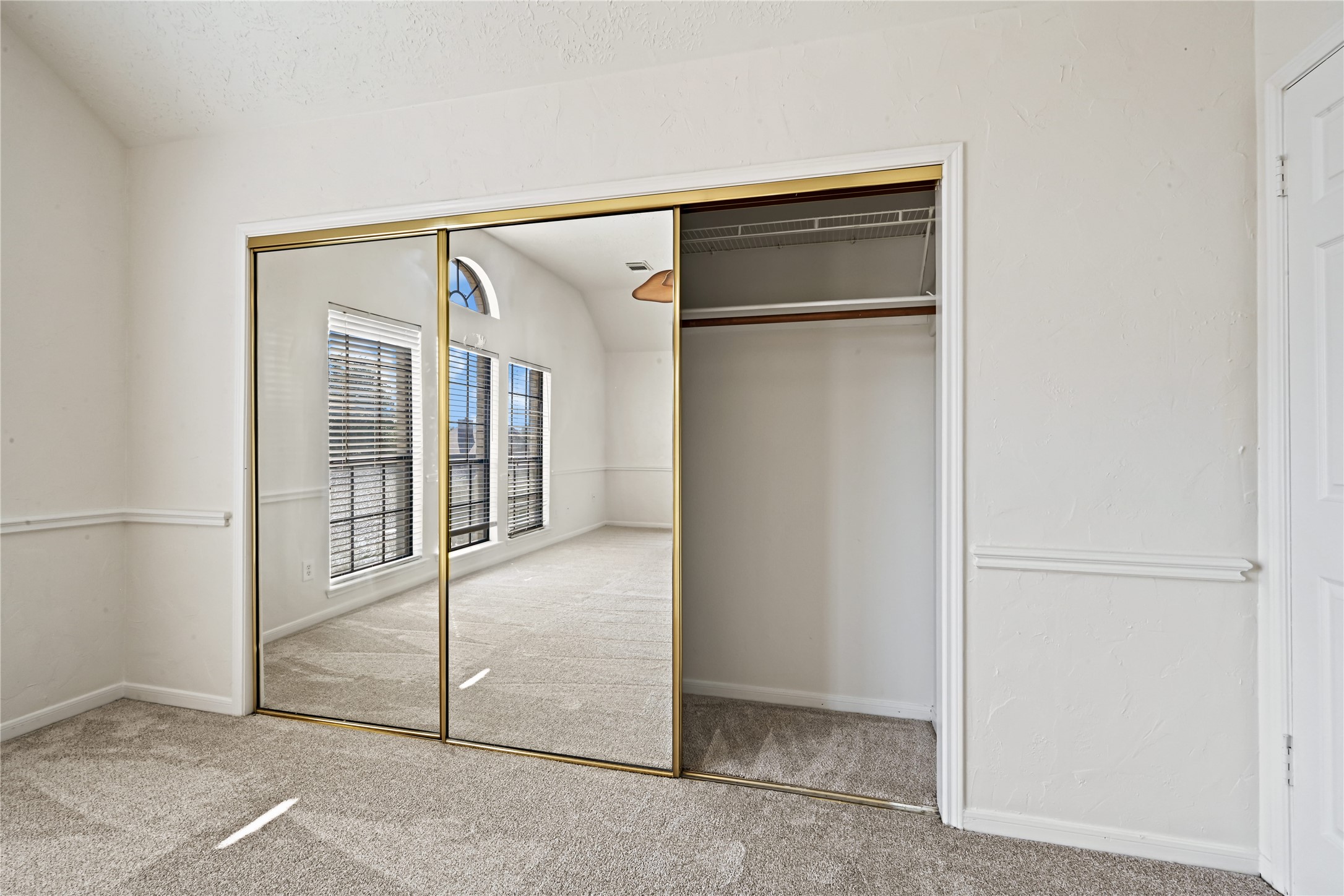 Spacious bedroom featuring a large mirrored closet, plush carpeting, and abundant natural light through arched windows.