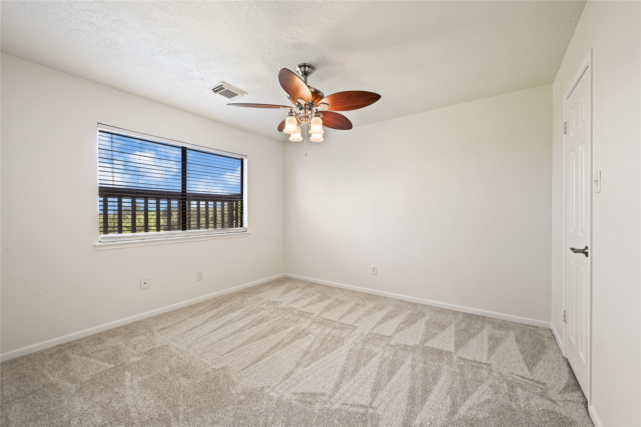 Bright and airy bedroom featuring plush carpet, a modern ceiling fan with lights, and a large window offering plenty of natural light.