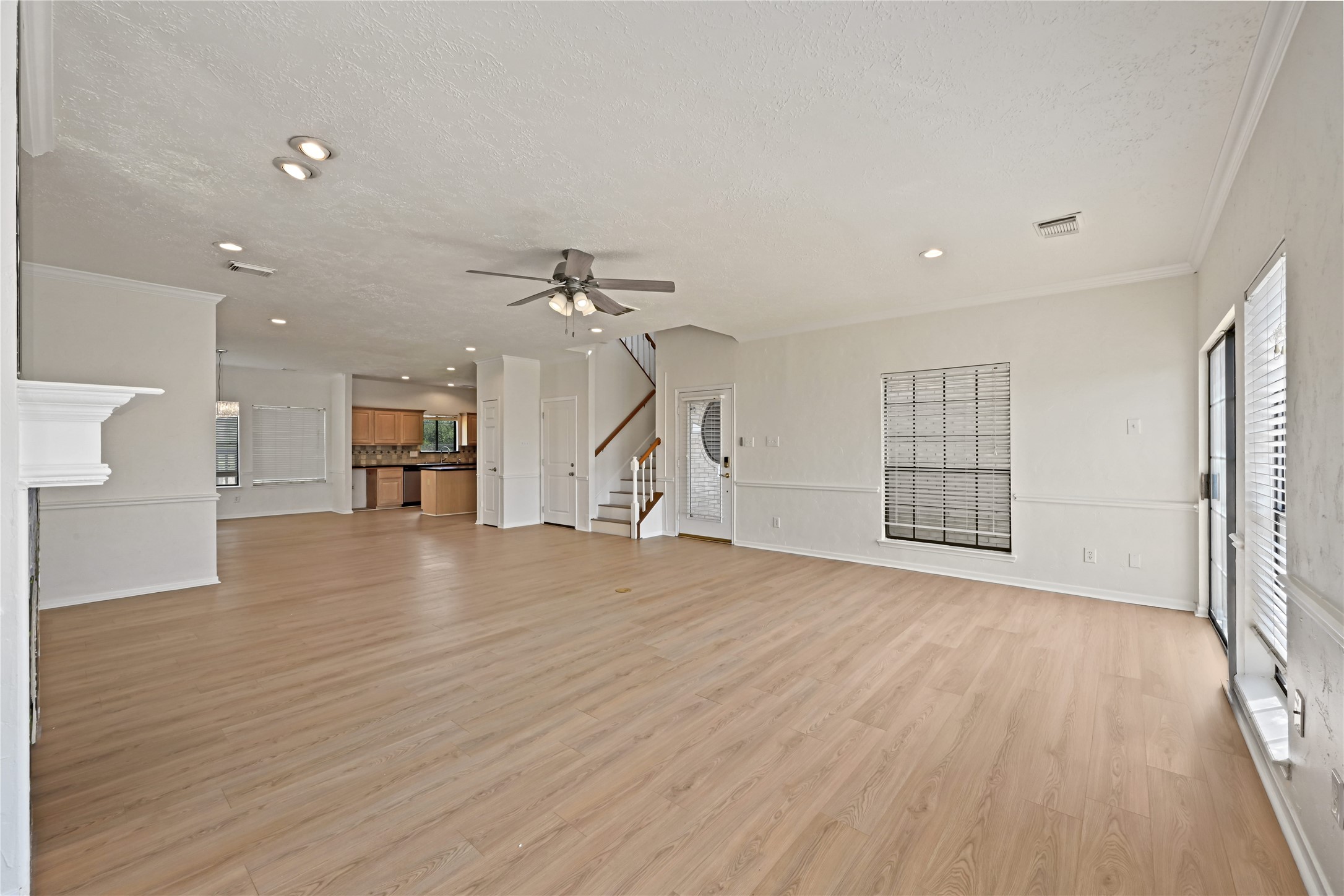 Lving area features elegant wood flooring, recessed lighting, and a ceiling fan, seamlessly connecting to a modern kitchen and featuring large windows for ample natural light.