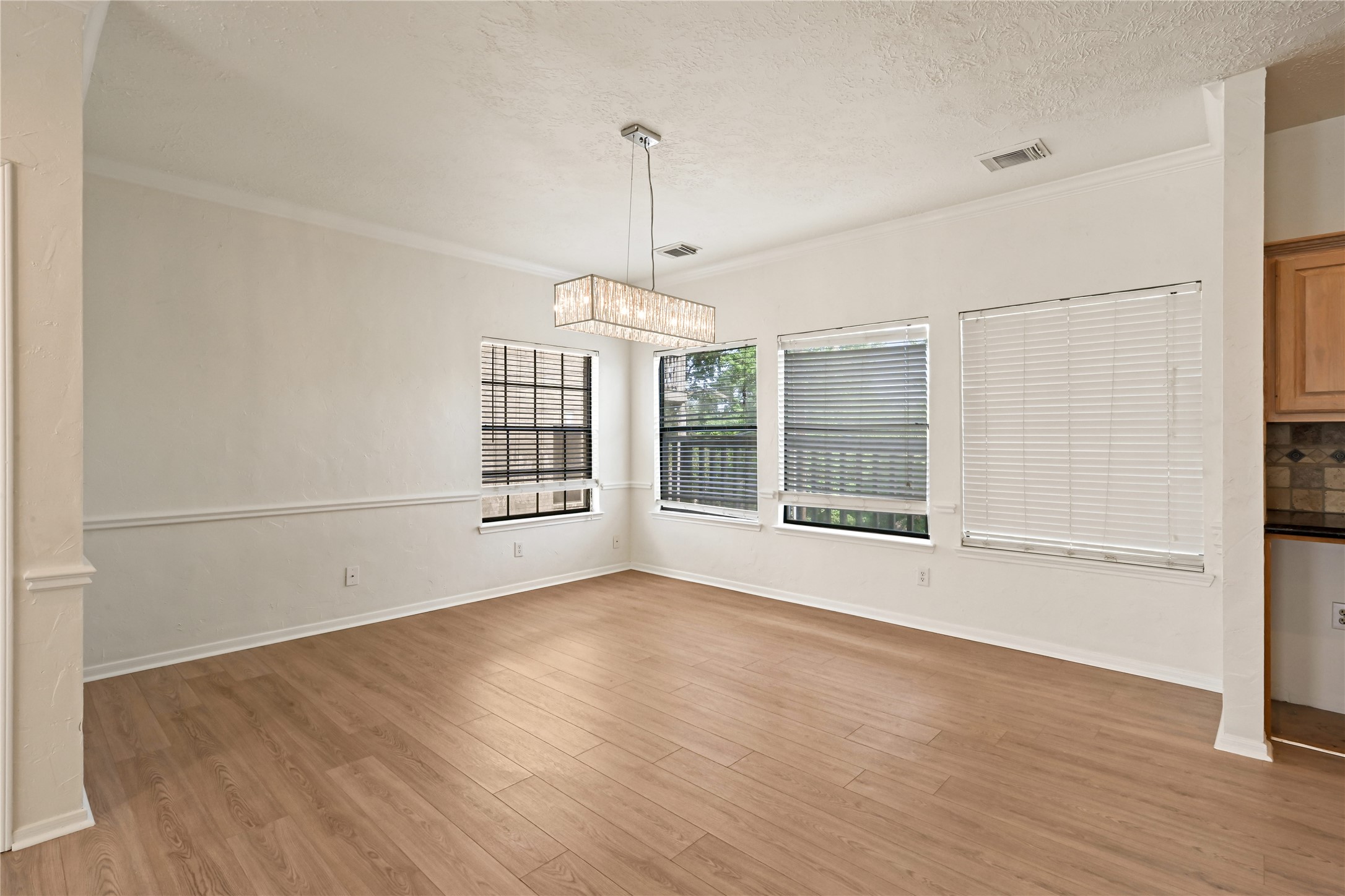 Bright dining area with elegant wood flooring, large windows for natural light, and a modern chandelier, offering a perfect space for gatherings.