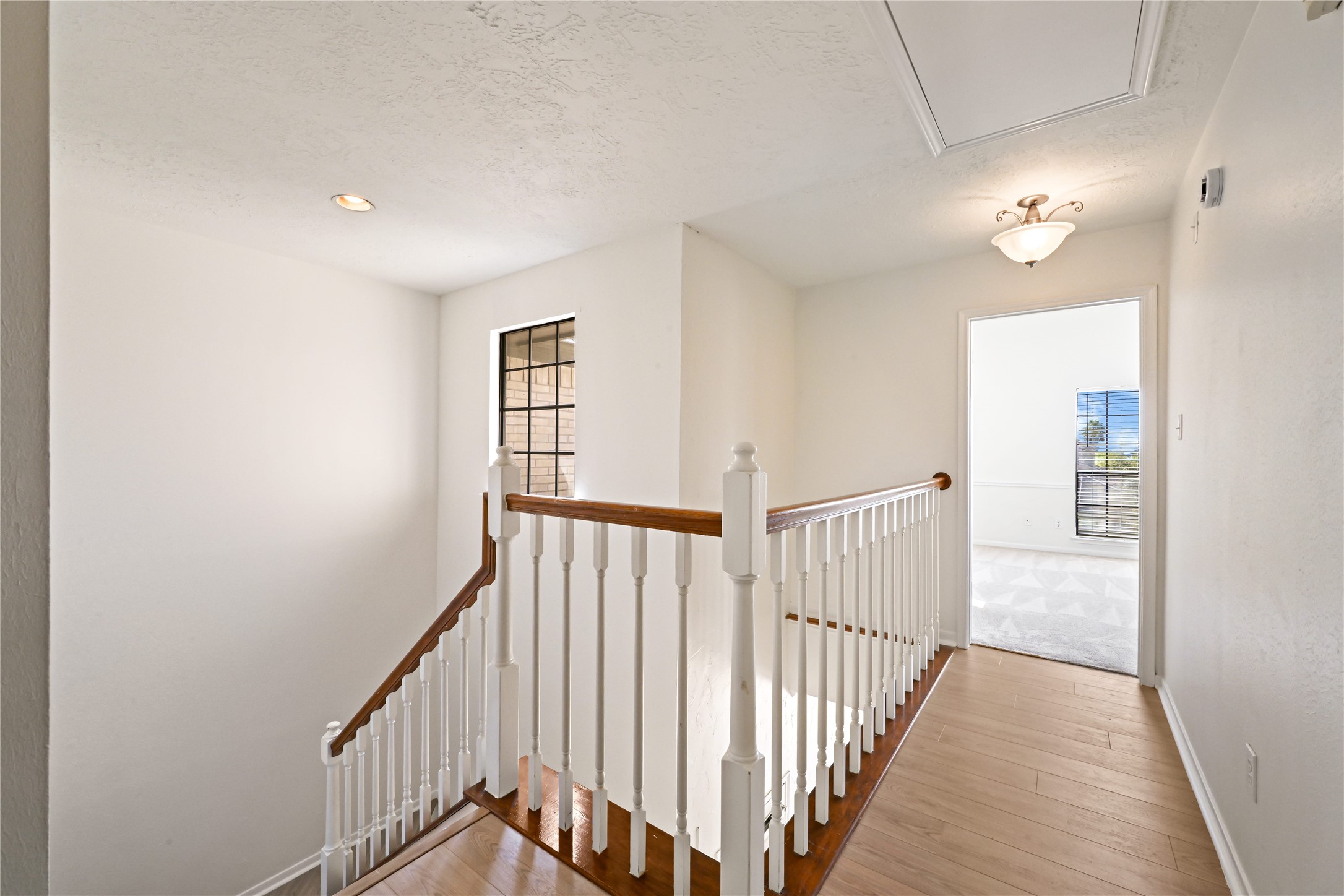 Bright and airy upstairs landing with elegant wood flooring and a classic railing, leading to a well-lit room with large windows.