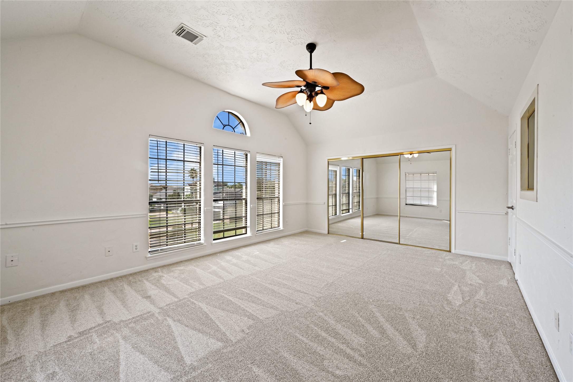 Spacious bedroom with vaulted ceiling, featuring large windows for ample natural light, plush carpeting, and mirrored closet doors for added elegance.