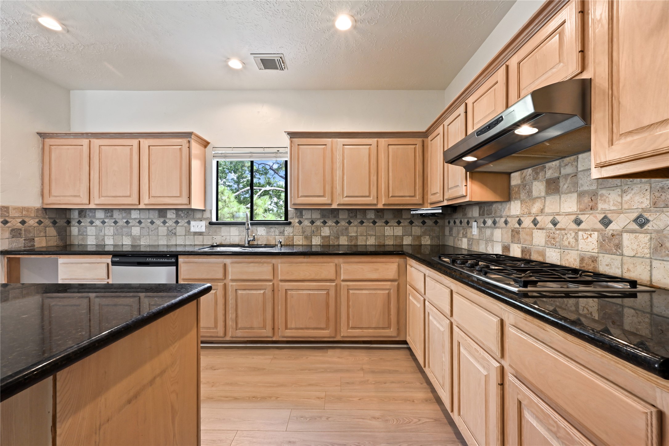 Spacious kitchen featuring natural wood cabinetry, sleek granite countertops, and a stylish tile backsplash.
