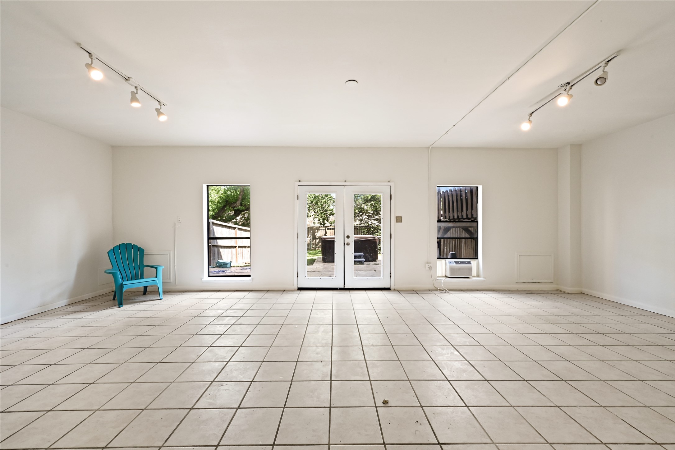 Ample space in this bright room with large tile flooring, featuring double doors leading to an inviting outdoor space.