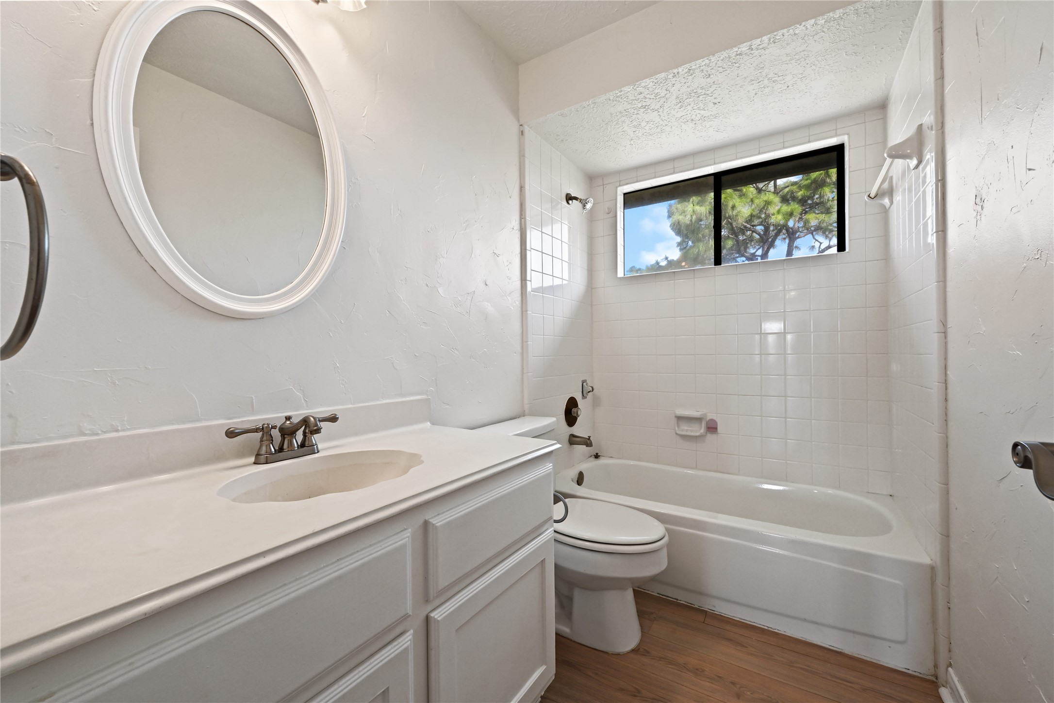 Bright and airy bathroom featuring a sleek white vanity, a classic bathtub with a window view, and elegant wood flooring.