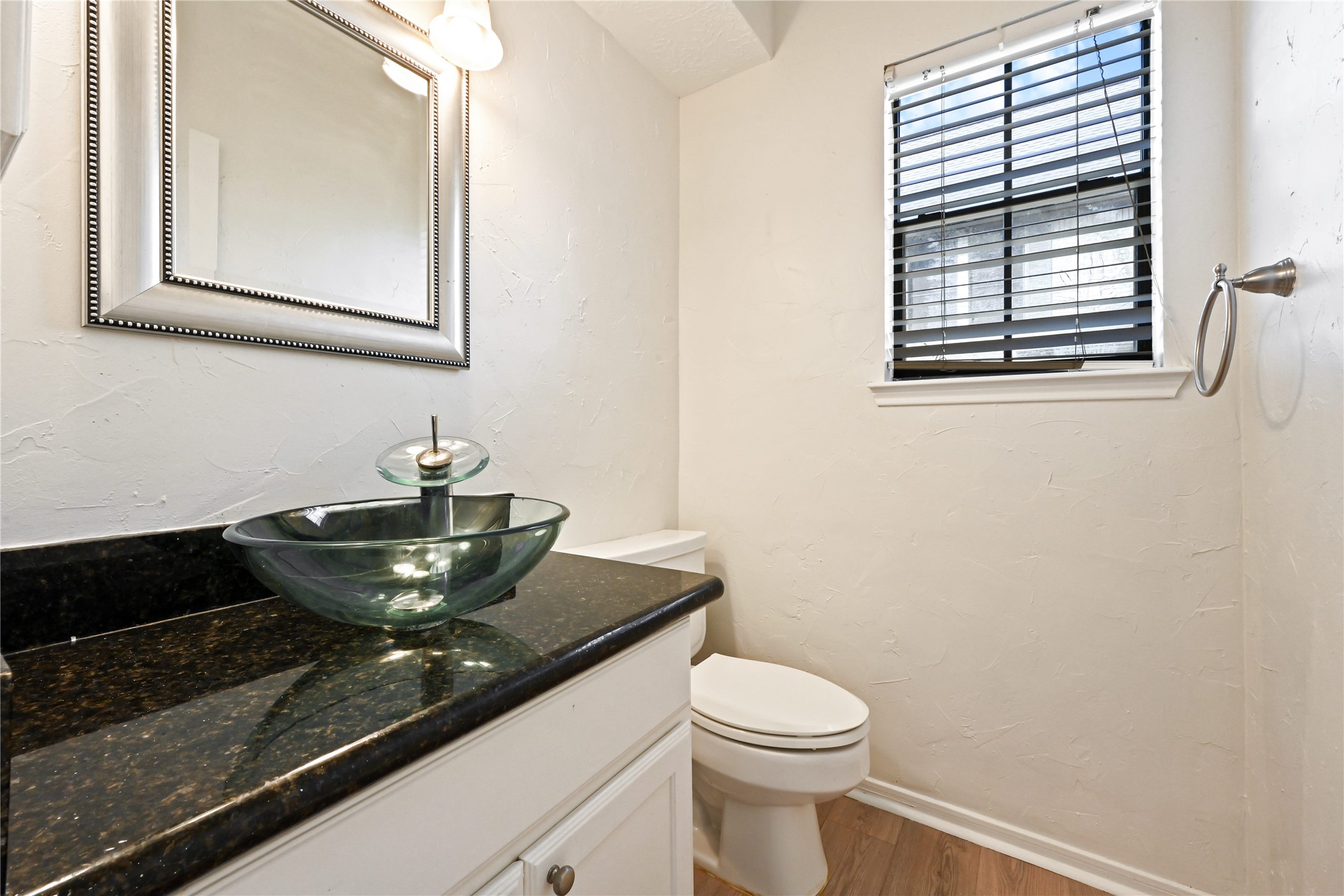 Chic powder room featuring a modern glass vessel sink, elegant black granite countertop, and soft natural light streaming through the window with stylish blinds.