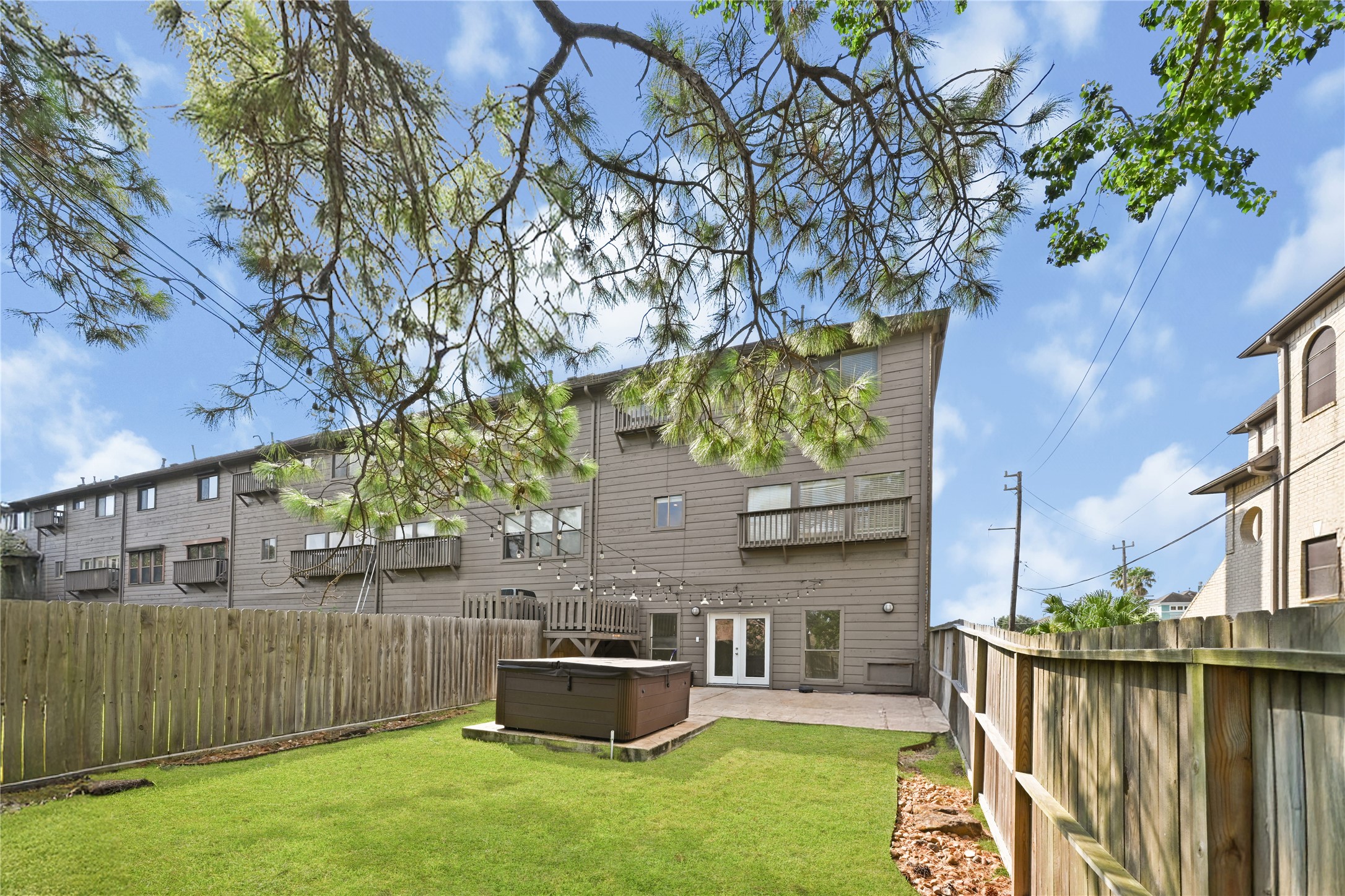 Expansive backyard with a patio and hot tub, enclosed by a wooden fence, perfect for outdoor relaxation and entertaining.