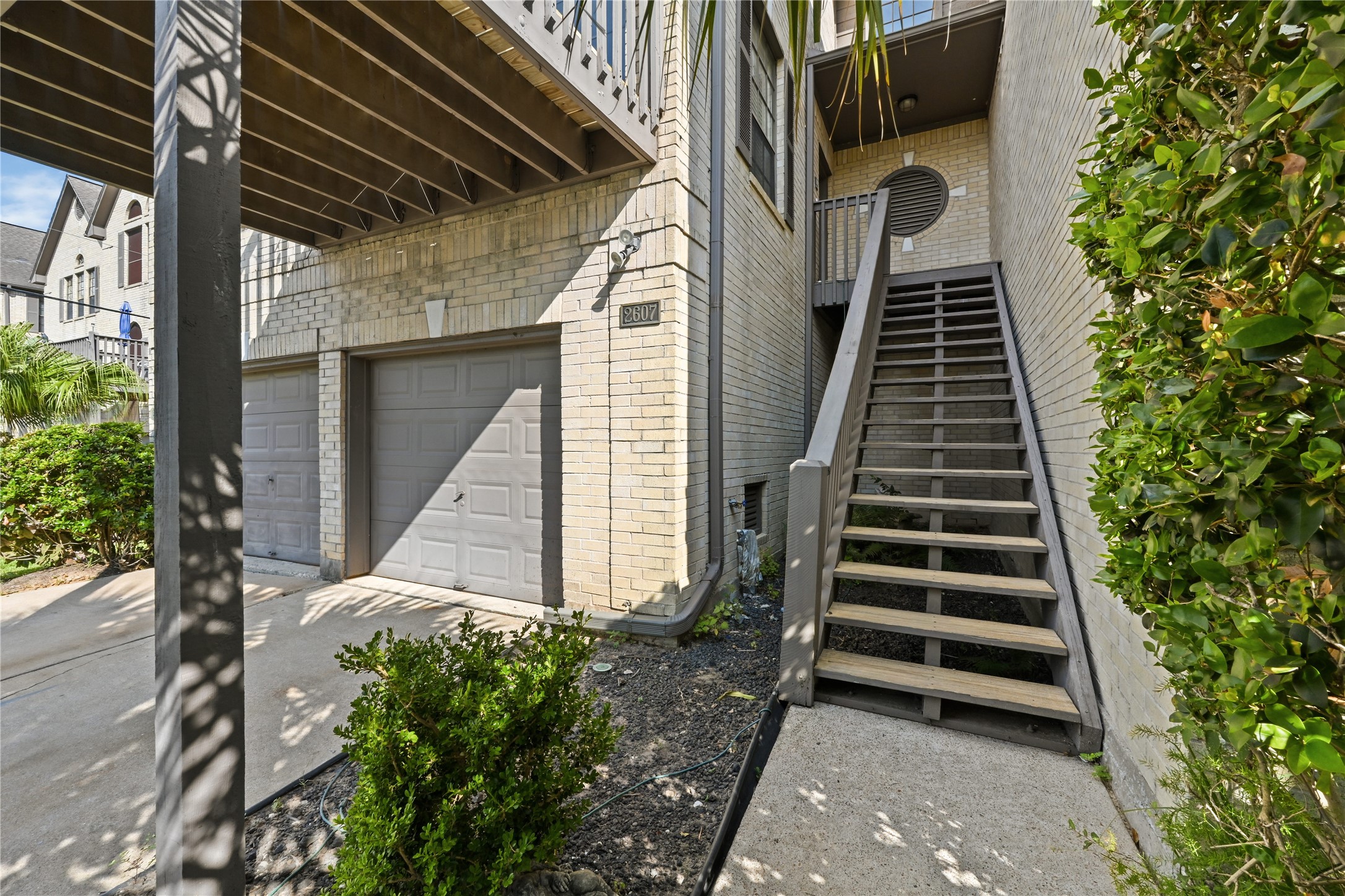 Charming two-story home with a spacious two-car garage and inviting wooden staircase leading to the main entrance, surrounded by lush greenery.