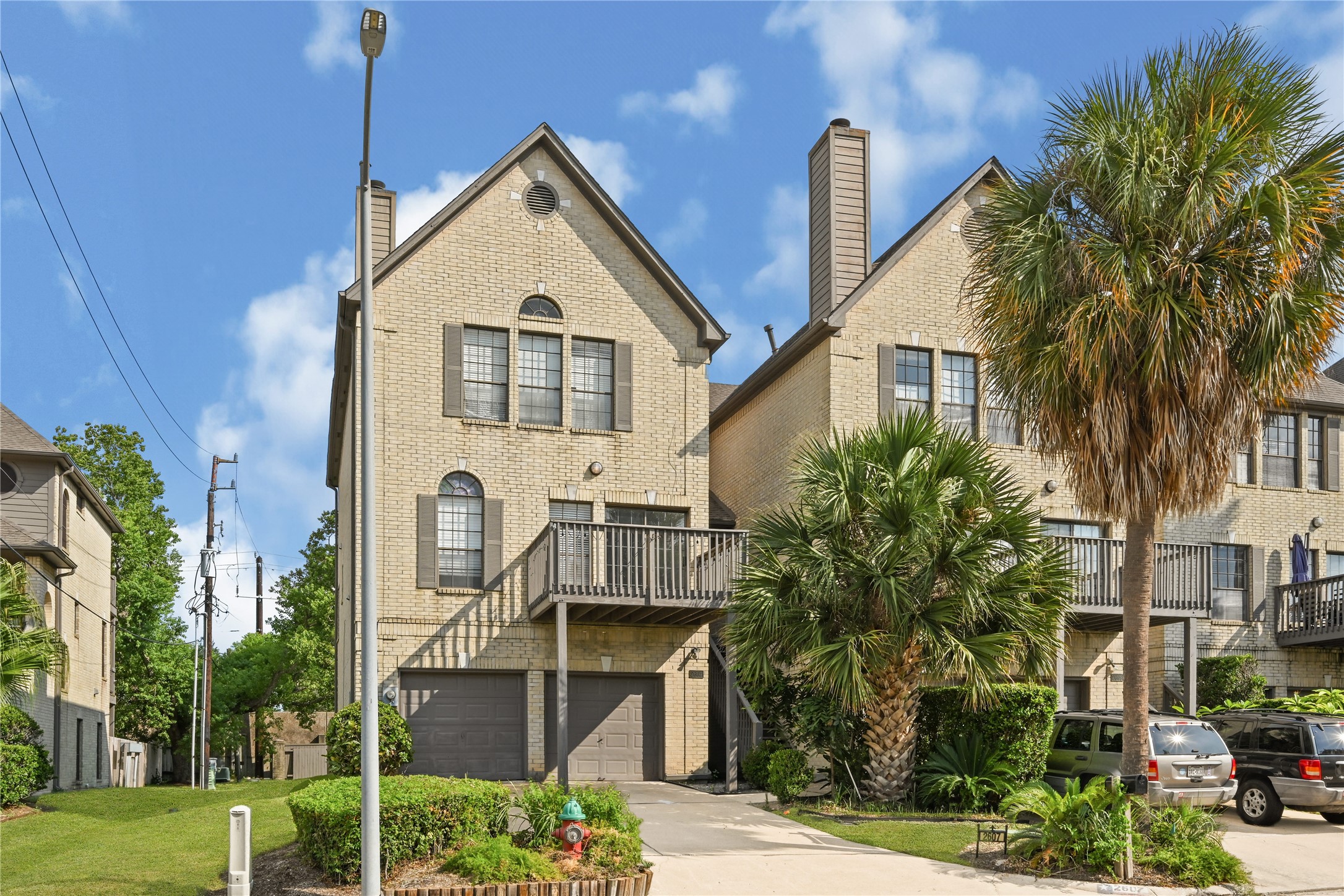 Charming townhouse with a brick exterior, featuring a spacious deck and lush palm trees, offering a blend of elegance and tropical charm.