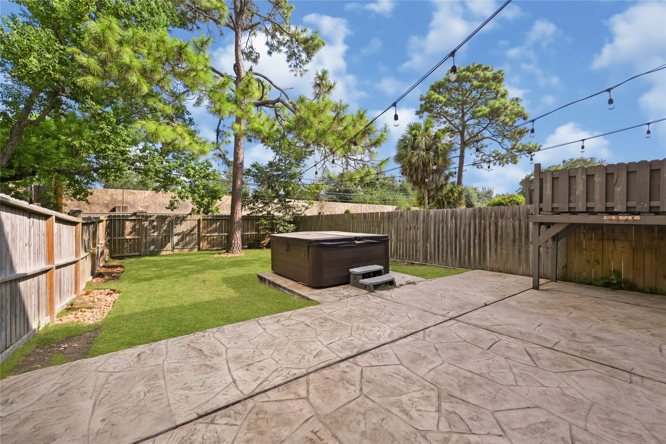 Charming backyard oasis featuring a spacious stamped concrete patio, a relaxing hot tub, and lush greenery surrounded by a privacy fence, perfect for outdoor entertaining.