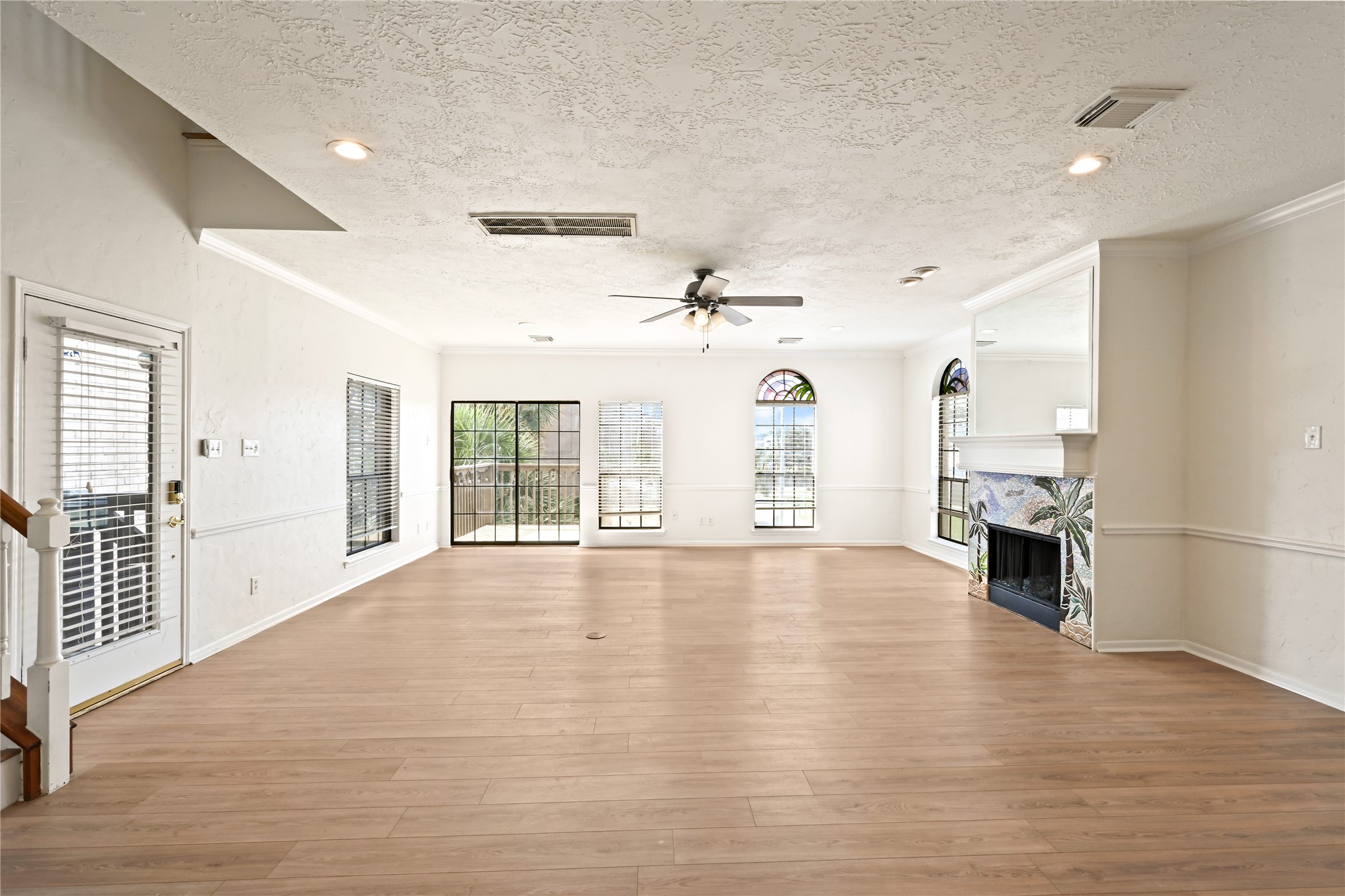 Spacious living area with abundant natural light, featuring elegant wood flooring, a decorative fireplace, and large windows offering scenic views.