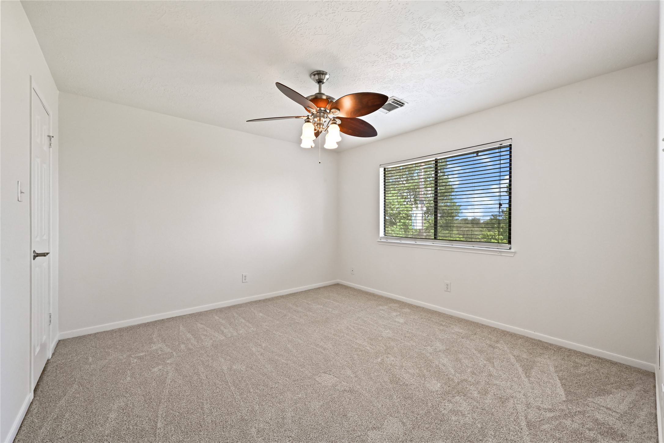 Spacious bedroom with soft carpet flooring, a ceiling fan, and a large window providing abundant natural light.