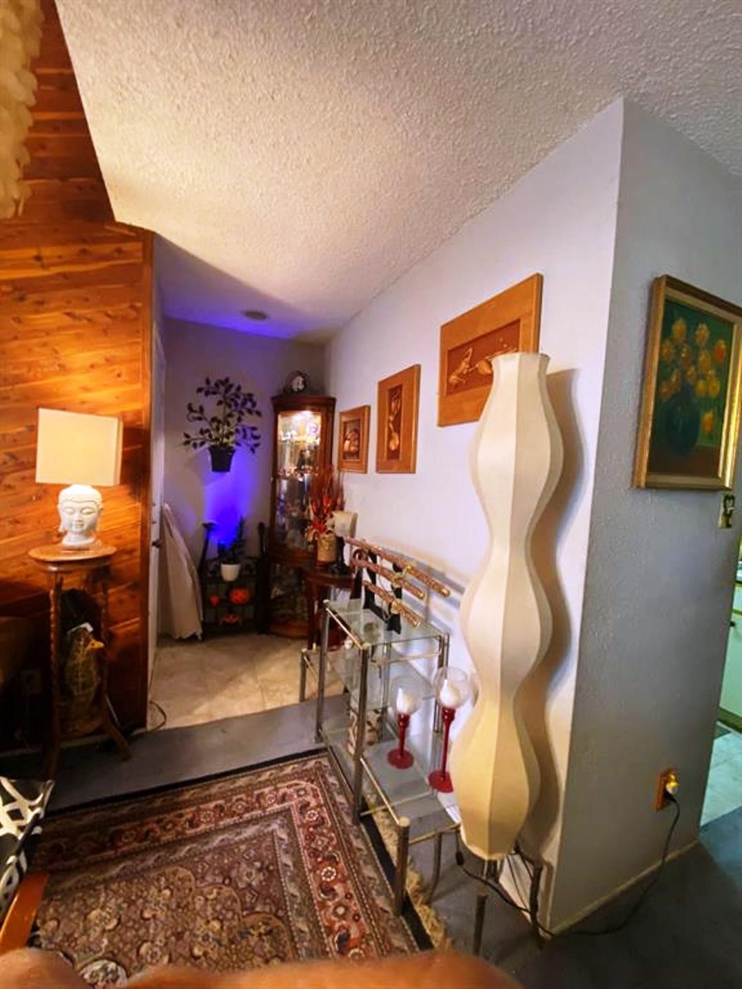 Cozy corner with a blend of wood and light-colored walls, featuring eclectic decor, including art pieces and a unique wavy lamp. The space has a warm, inviting ambiance, enhanced by soft lighting and a decorative rug.