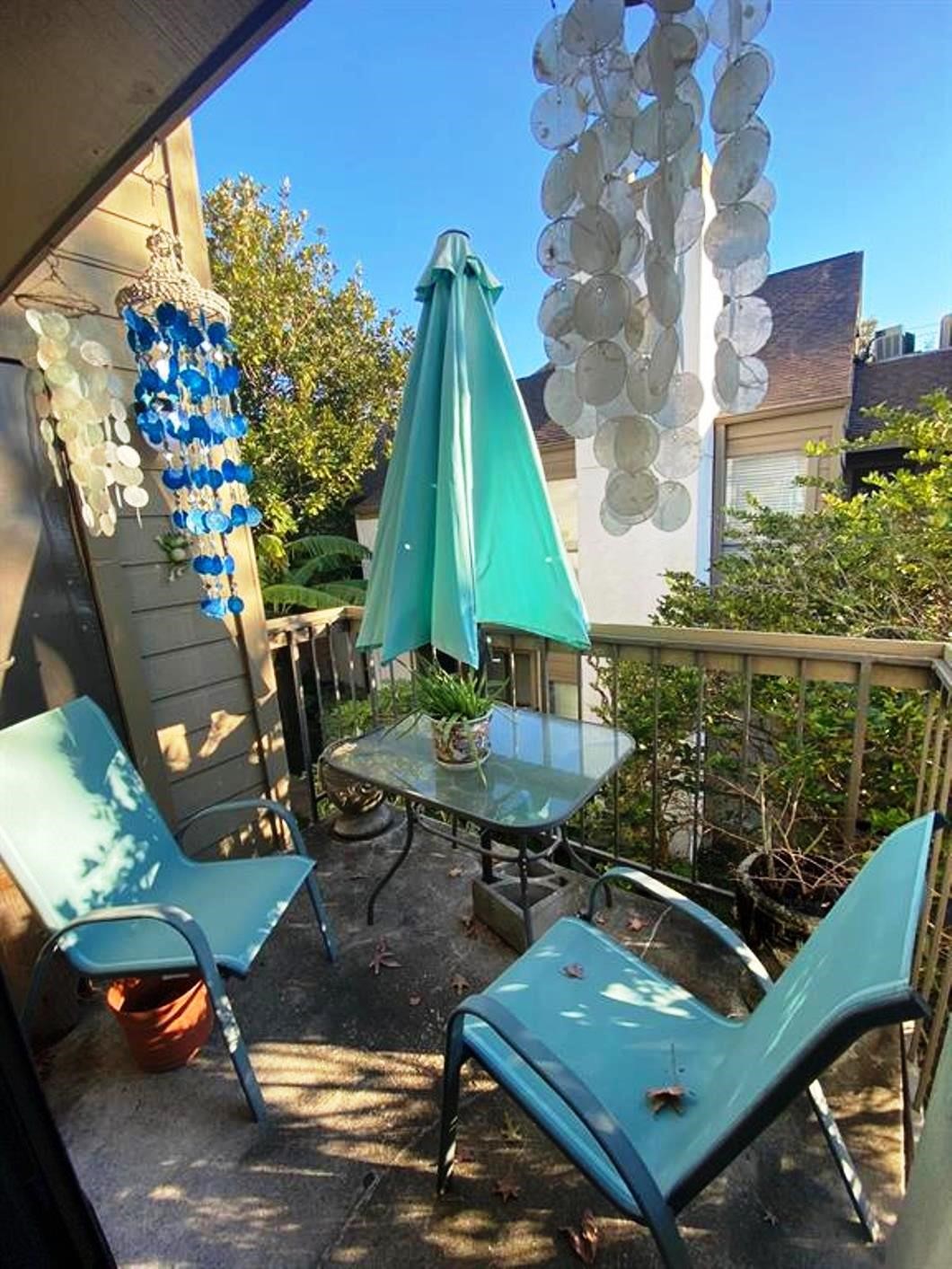 Cozy balcony with two chairs and a small glass table, perfect for relaxing. Decor includes hanging blue and white ornaments and a teal umbrella, creating a tranquil outdoor retreat.