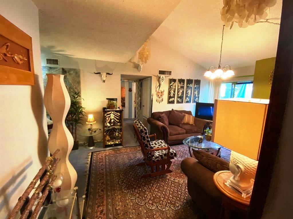 Cozy living room with warm lighting and eclectic decor. Features comfortable seating, a glass coffee table, and decorative wall art. The space has a welcoming ambiance with a mix of modern and rustic elements, perfect for relaxation.