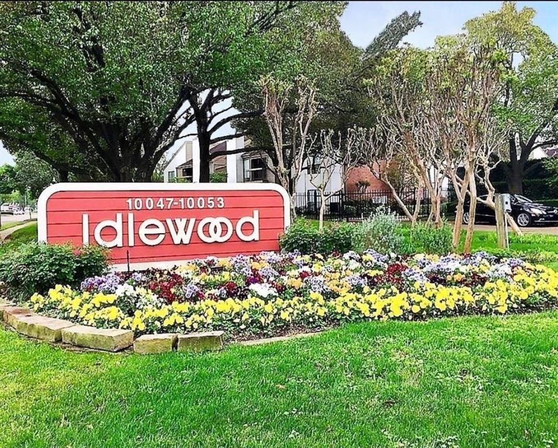 Charming entrance to a residential community, featuring a vibrant flower bed and a welcoming "Idlewood" sign framed by lush trees. Ideal for buyers seeking a picturesque neighborhood.