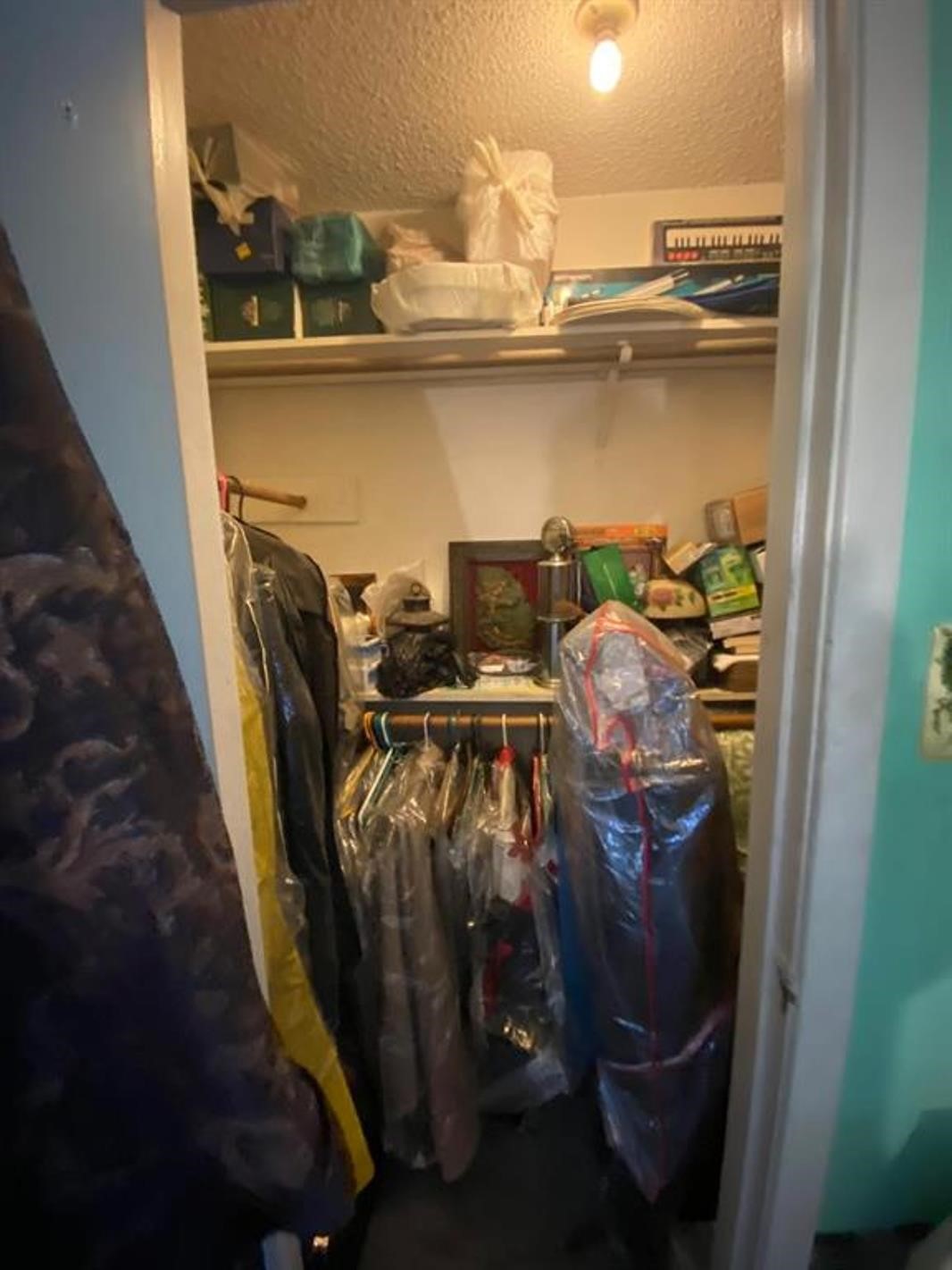 This is a small, well-lit closet with hanging space for clothes and shelves for storage, currently filled with various items.