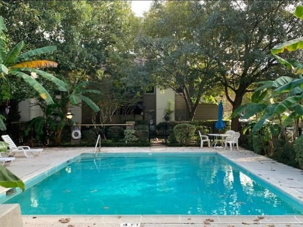 This photo showcases a serene backyard with a well-maintained pool surrounded by lush greenery. There's a seating area with a table and chairs, perfect for relaxing or entertaining.