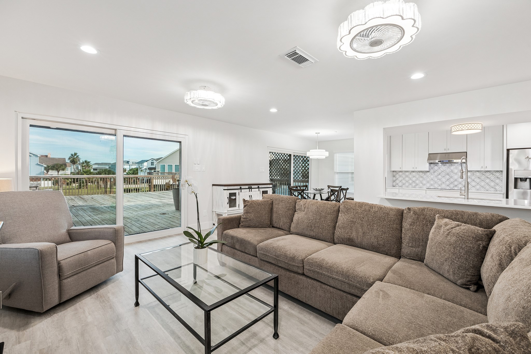 Experience serene living with this open-concept space, featuring neutral tones that seamlessly blend a cozy living area, modern kitchen, and expansive deck views.