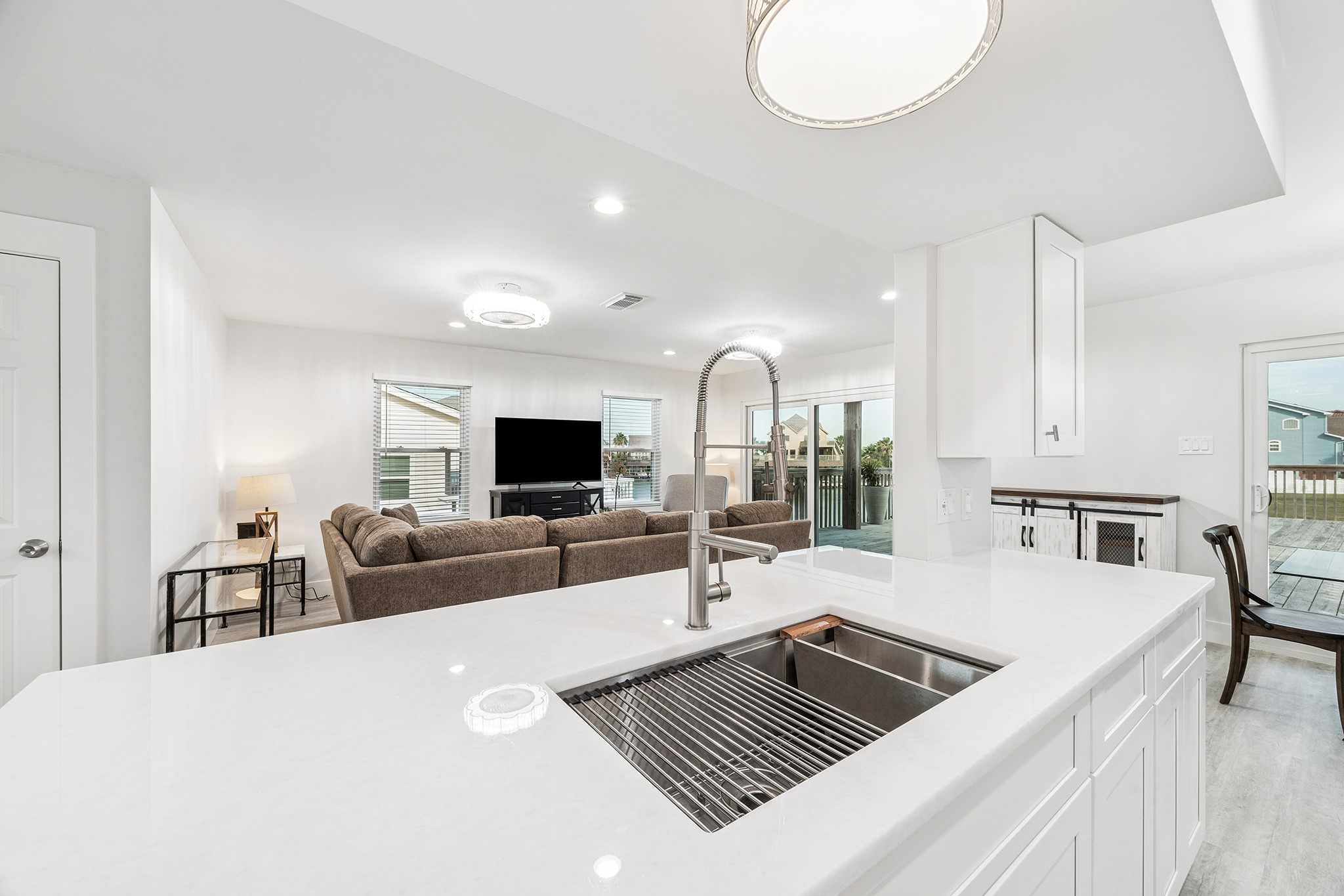 Discover a bright, open-concept living space where a sleek kitchen island with a modern sink seamlessly connects to a cozy living area, perfect for entertaining and enjoying natural light.