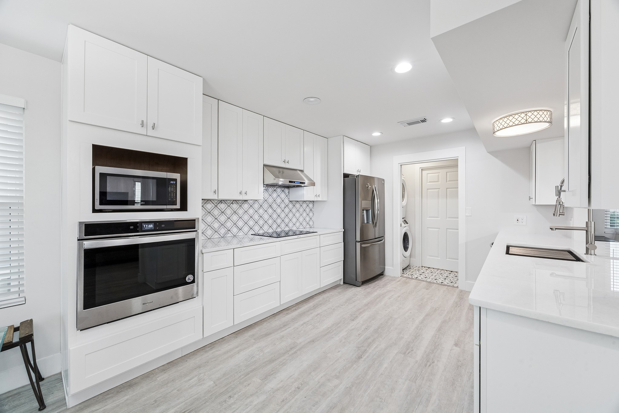 This sleek, modern kitchen boasts pristine white cabinetry, state-of-the-art stainless steel appliances, and an elegant tile backsplash, offering a bright and inviting space perfect for culinary creativity.