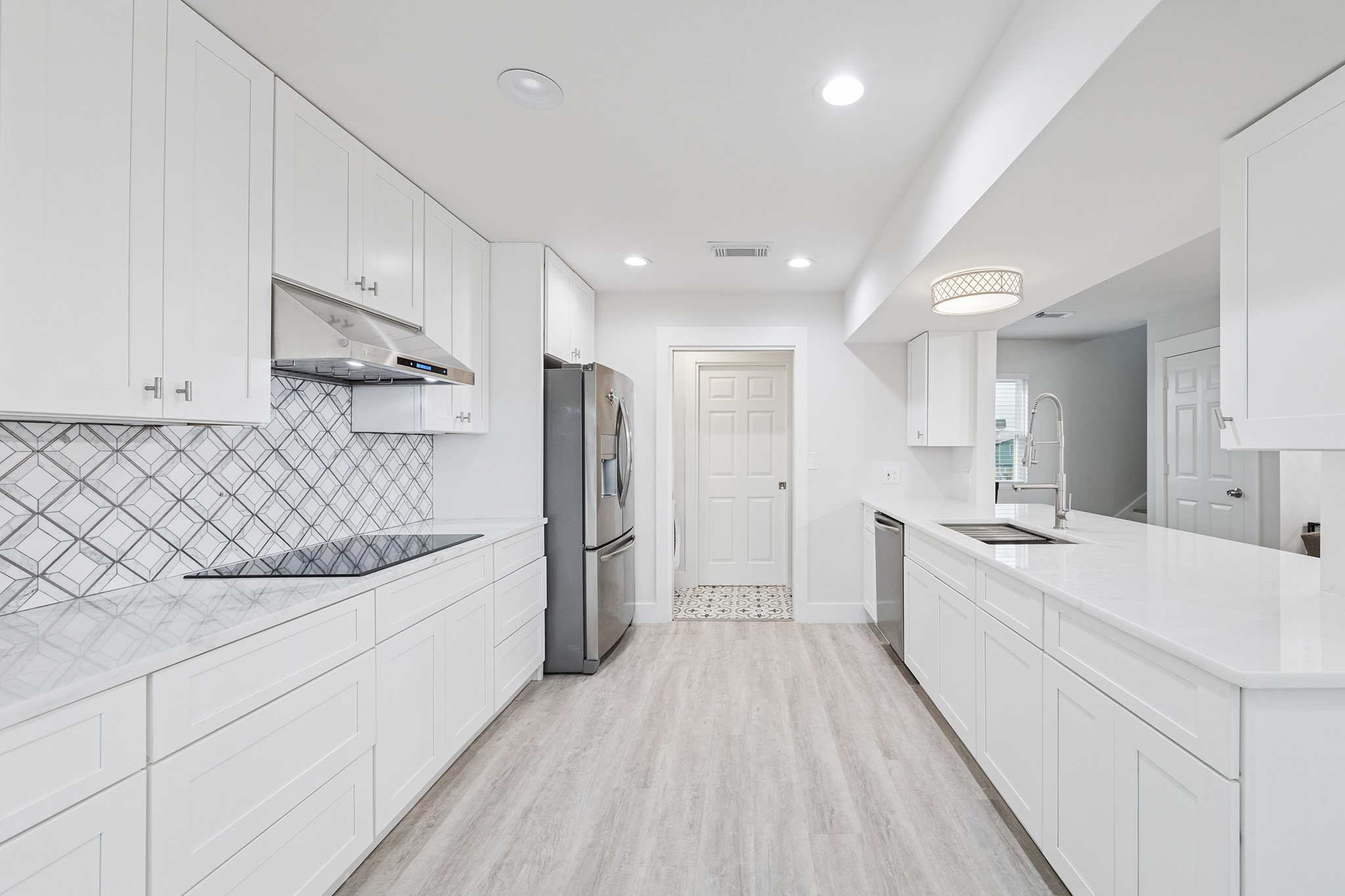 Discover culinary bliss in this sleek, modern kitchen featuring elegant white cabinetry, a chic geometric backsplash, and top-notch stainless steel appliances, all bathed in natural light.