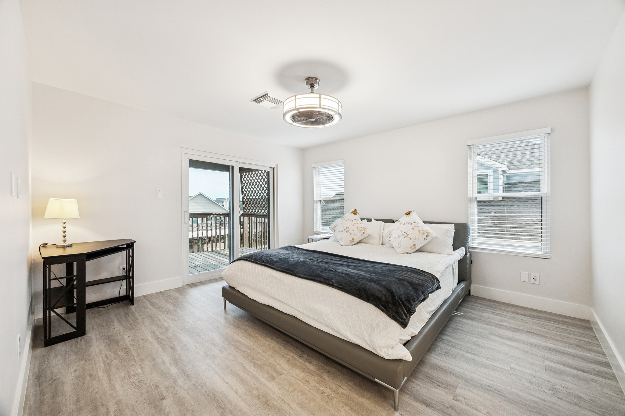 Discover your serene retreat in this bright and airy primary bedroom, featuring sleek flooring, a modern light fixture, and sliding doors that open to a private deck for seamless indoor-outdoor living.