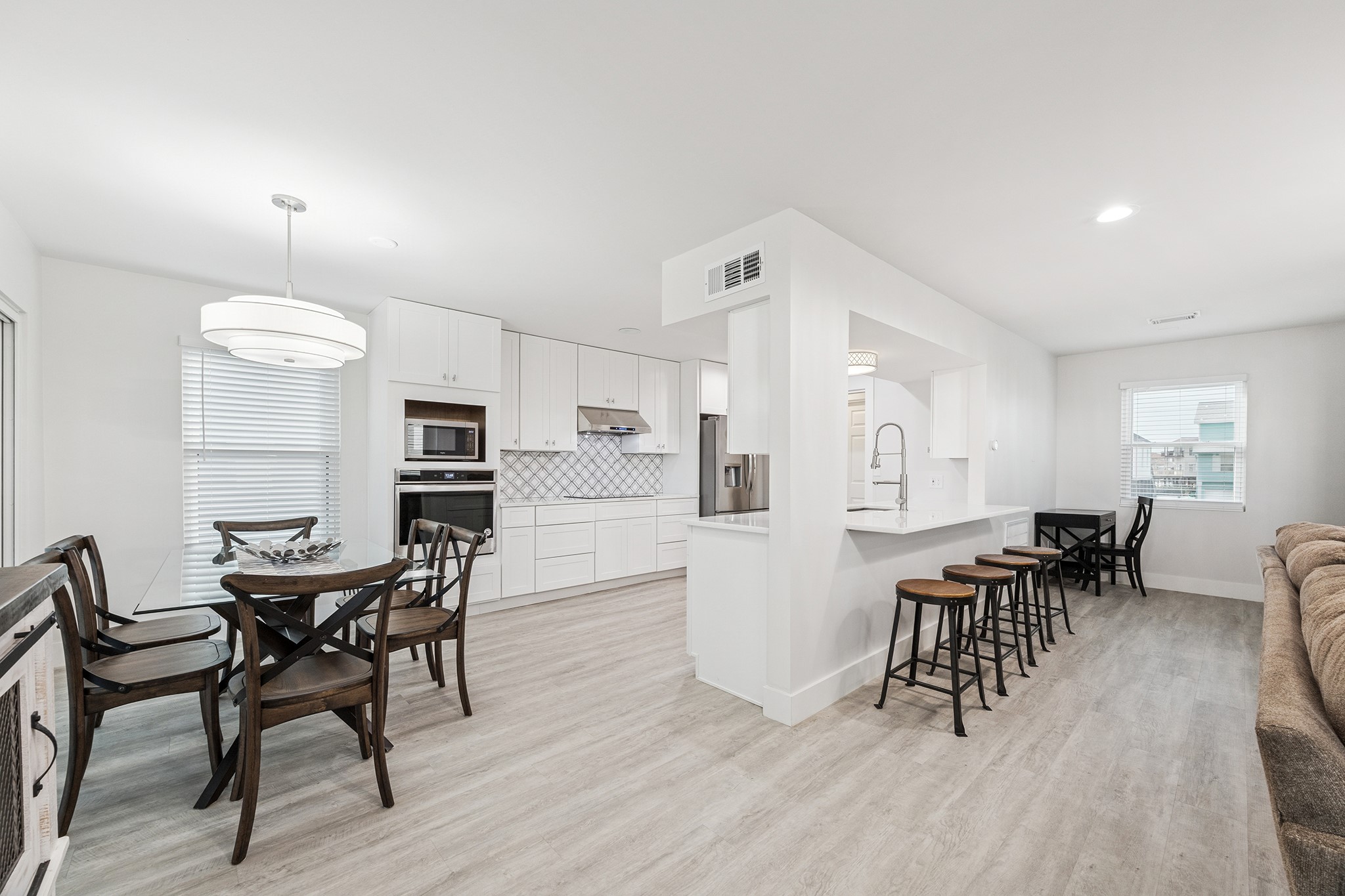 This bright and modern kitchen-dining area features sleek white cabinetry, a spacious breakfast bar with seating, and an inviting dining space perfect for entertaining.
